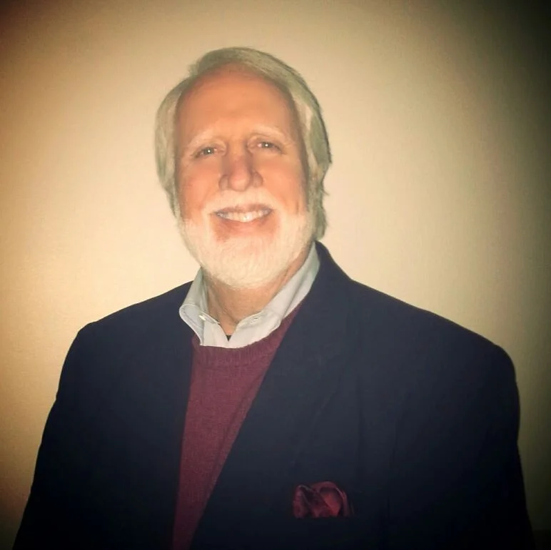 Joe James with a beard and hair, wearing a collared shirt and blazer.