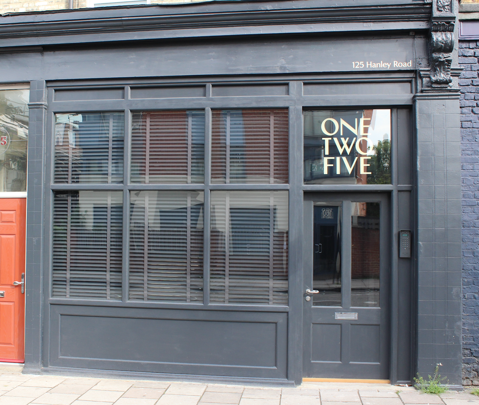 Black storefront with large window and door, displaying the address 125 Hanley Road and the text ONE TWO FIVE in white letters on the window.