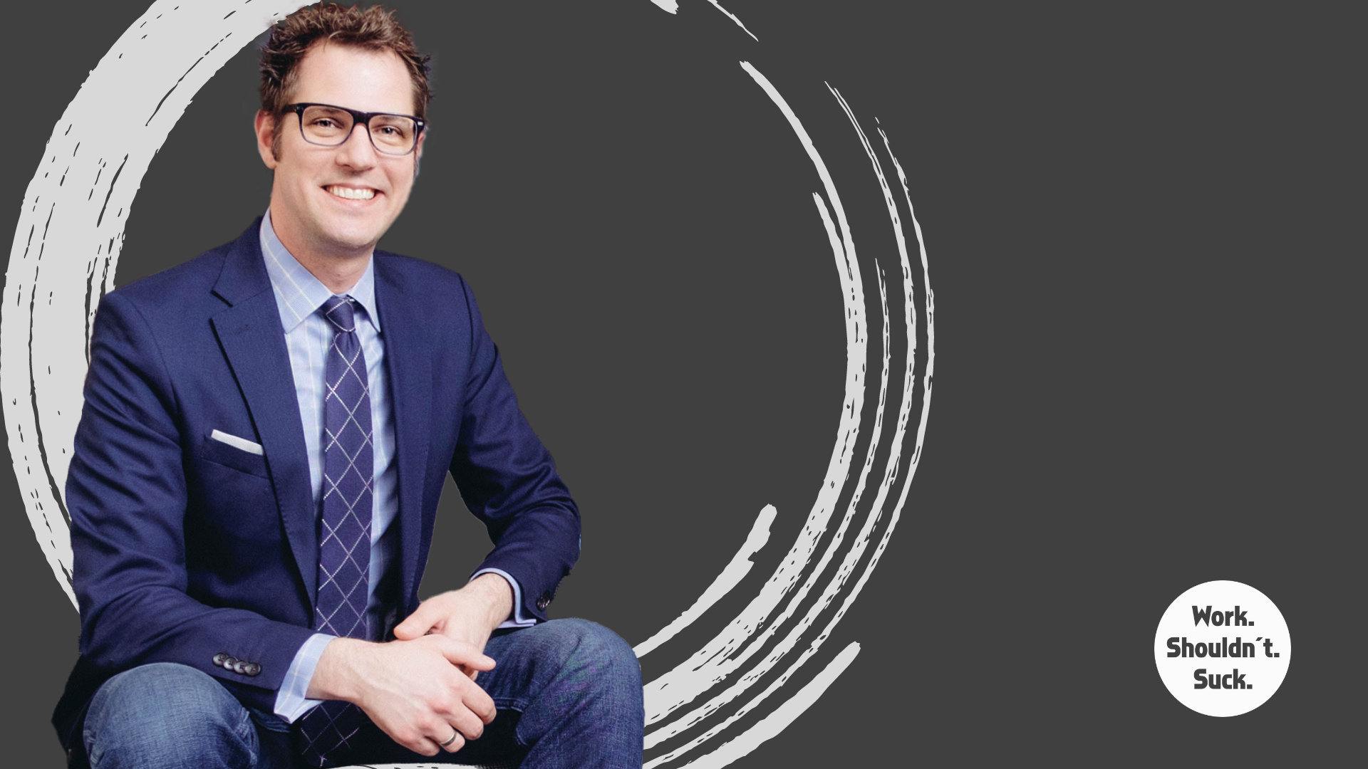 Man in a navy suit and glasses sitting with a dark circular design in the background and text 'Work. Shouldn't. Suck.'
