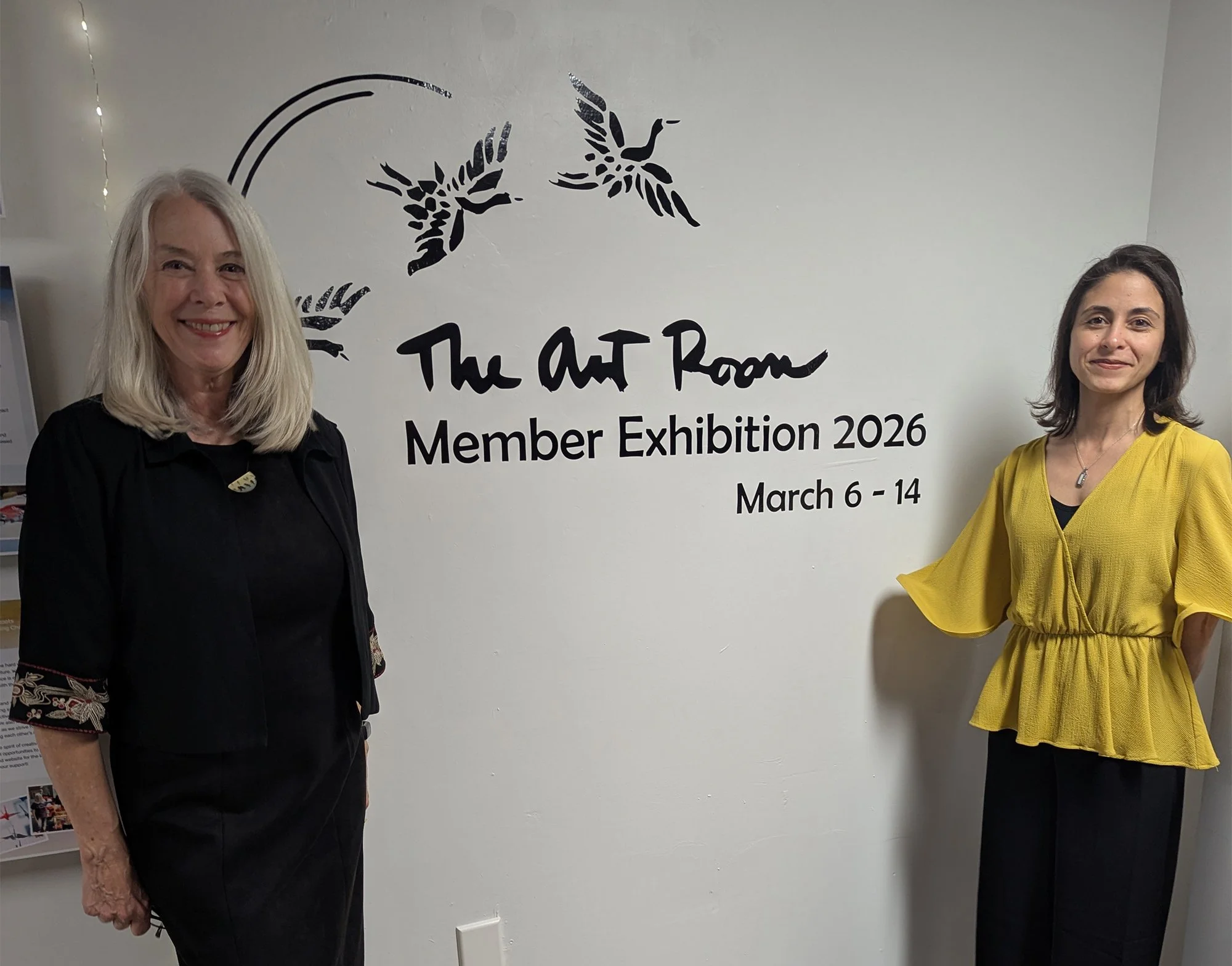 Marlys Lamar and Maryam Flory stand by a sign that reads The Art Room Member Exhibition 2026 March 6-14