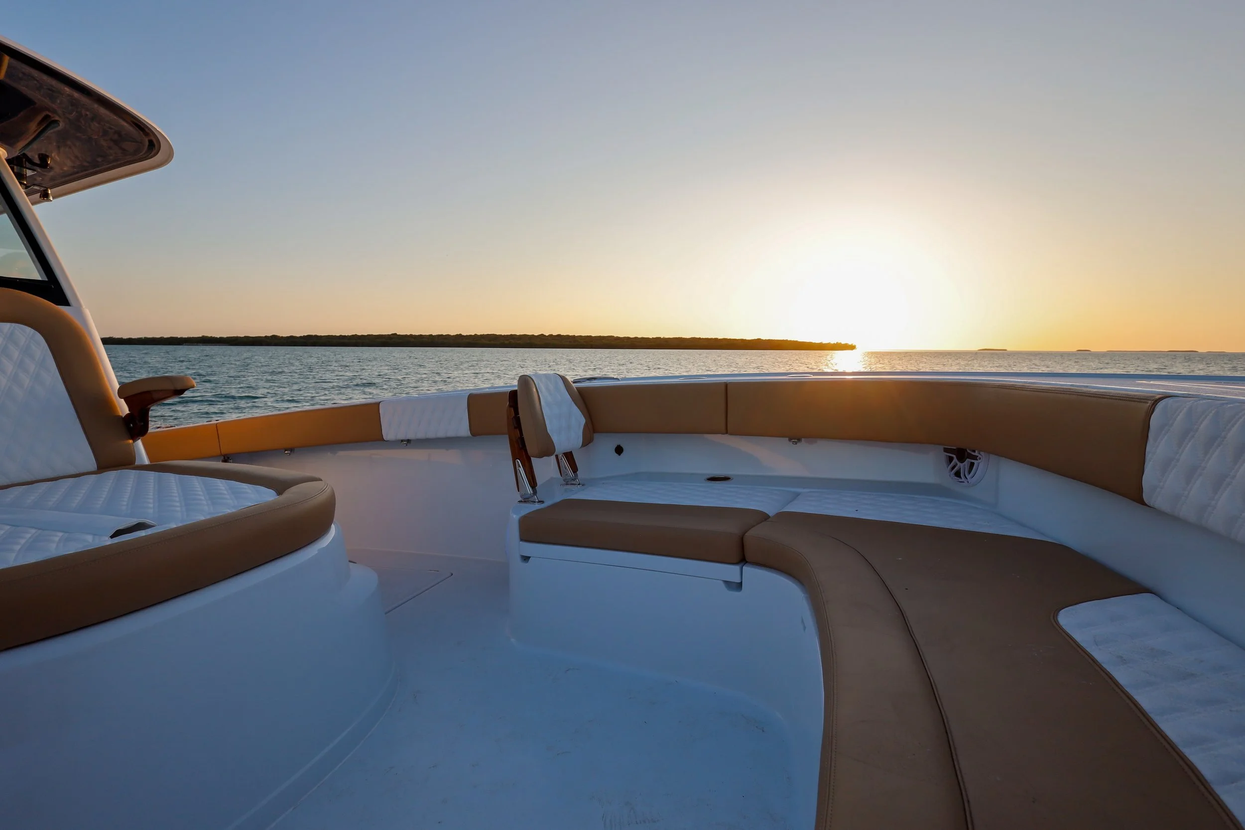 View of a boat's deck with cushioned seating, overlooking a body of water at sunset.