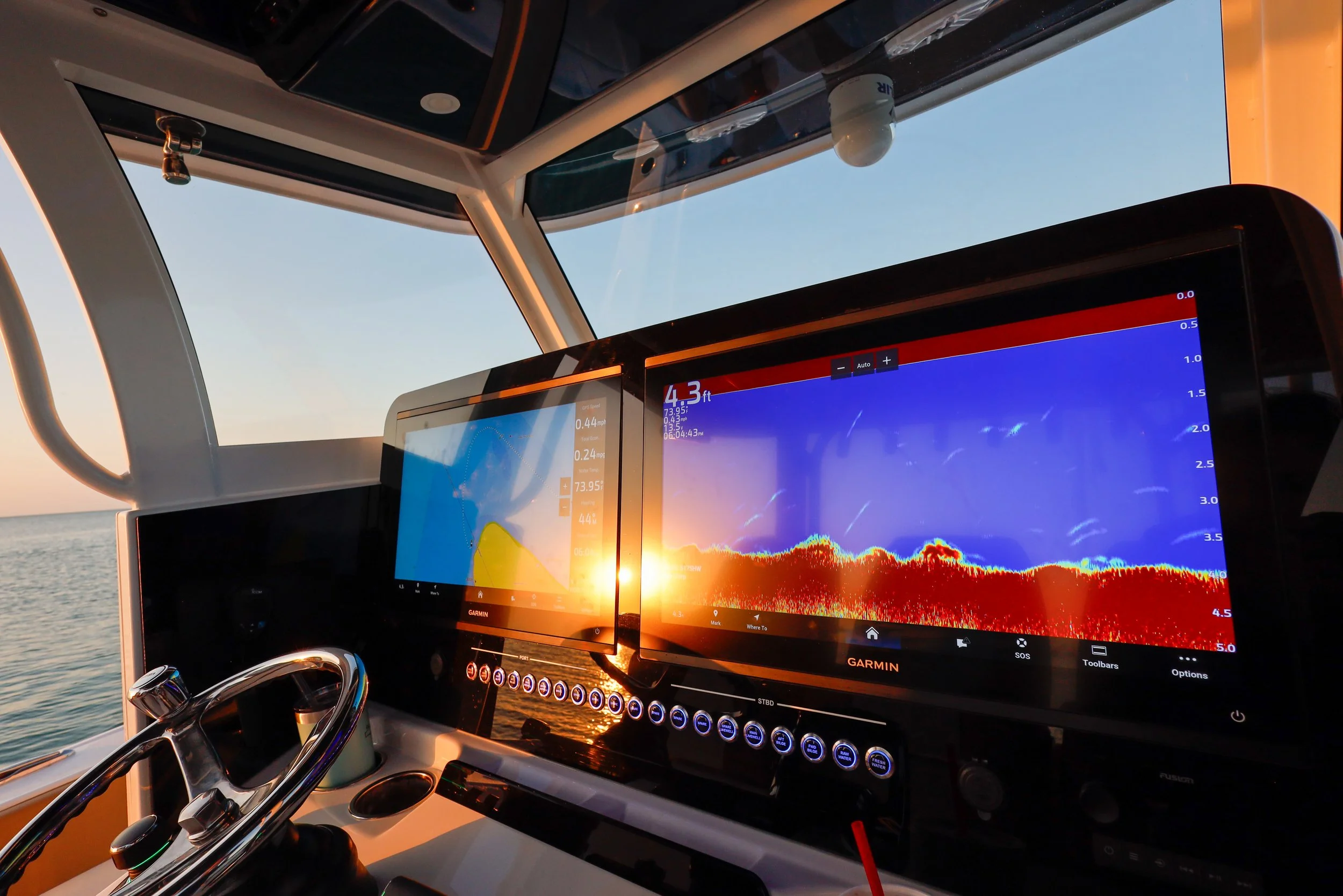 Boat cockpit at sunset with two Garmin fish finders showing underwater sonar readings and navigation data.