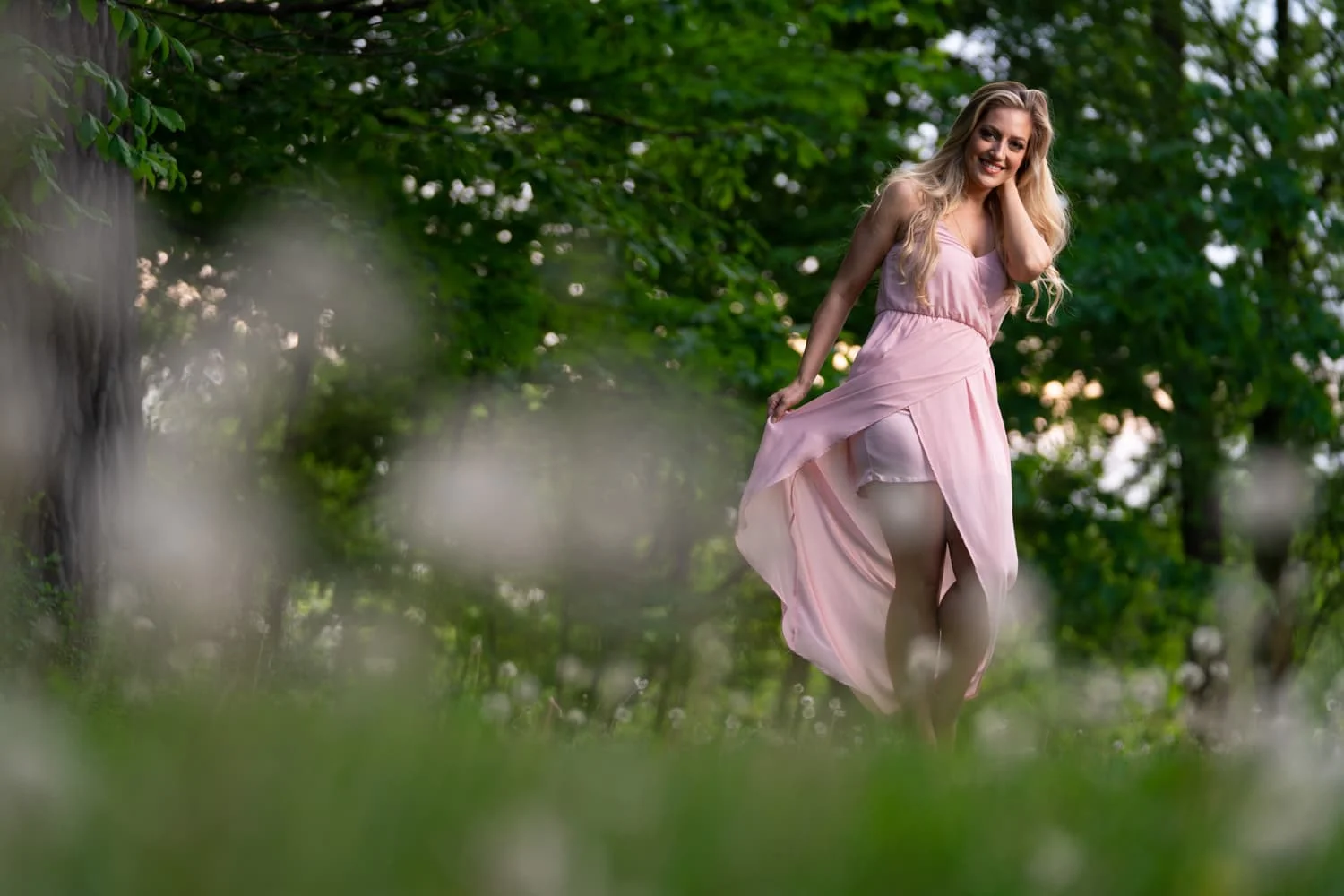 Blonde woman twirling pink dress in field of dandelions