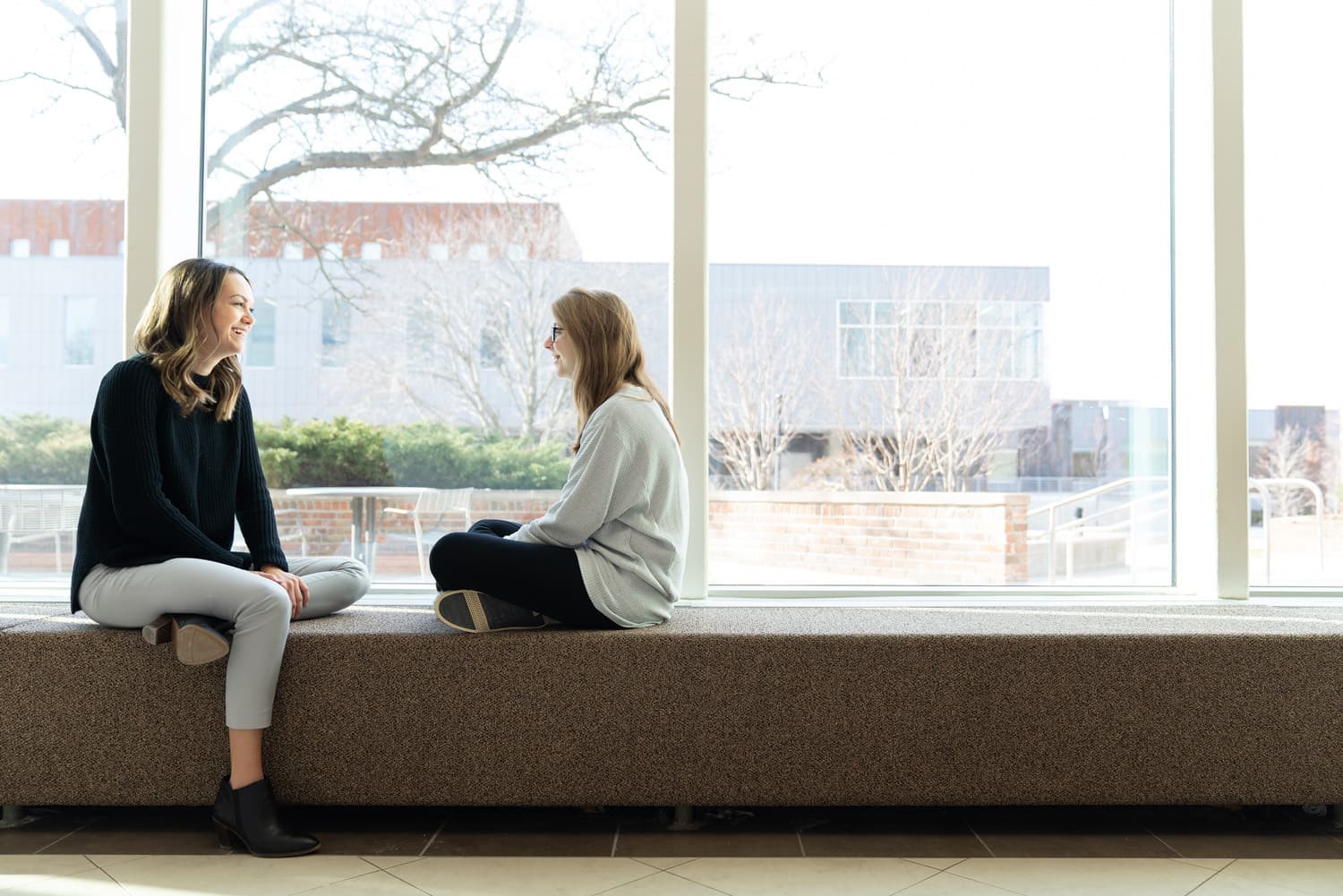  student and advisor sitting and talking near windows 