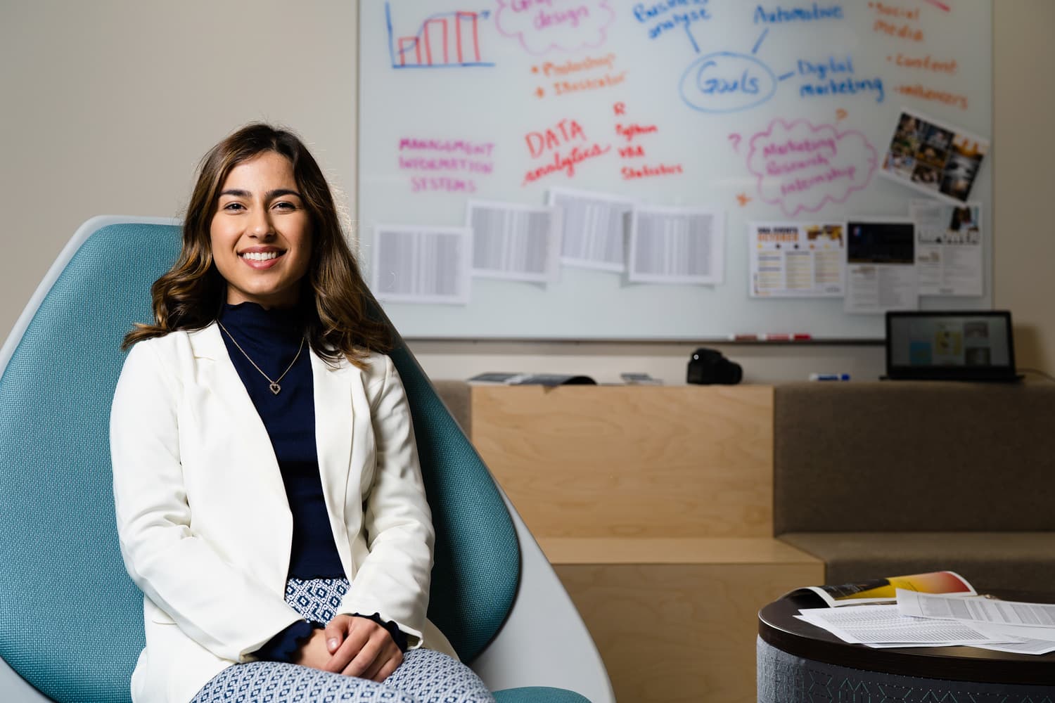  student in white coat sitting in blue chair in front of whiteboard 
