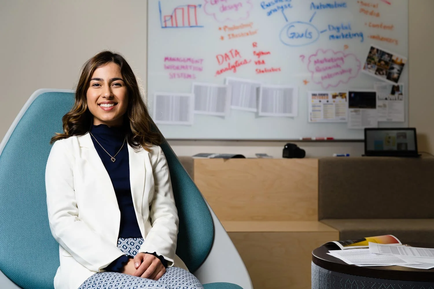 student in white coat sitting in blue chair in front of whiteboard