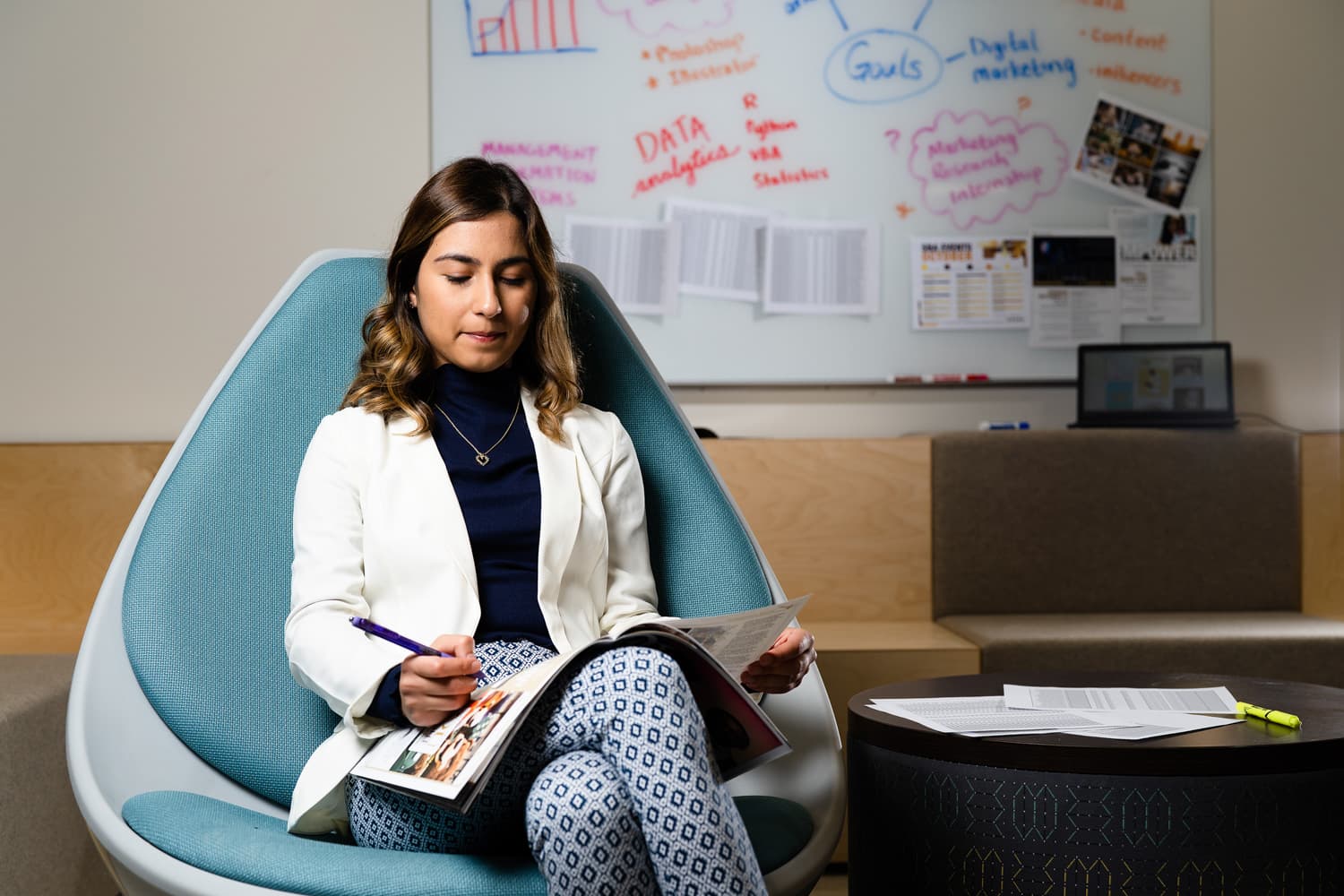  student in white coat sitting in blue chair writing 