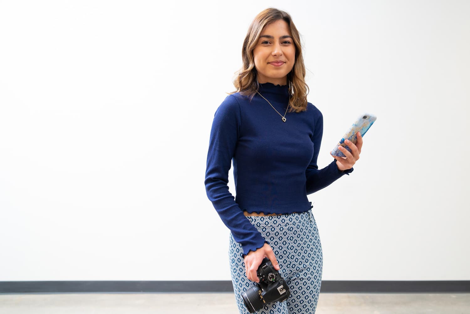  student holding phone and dslr camera in front of white background 