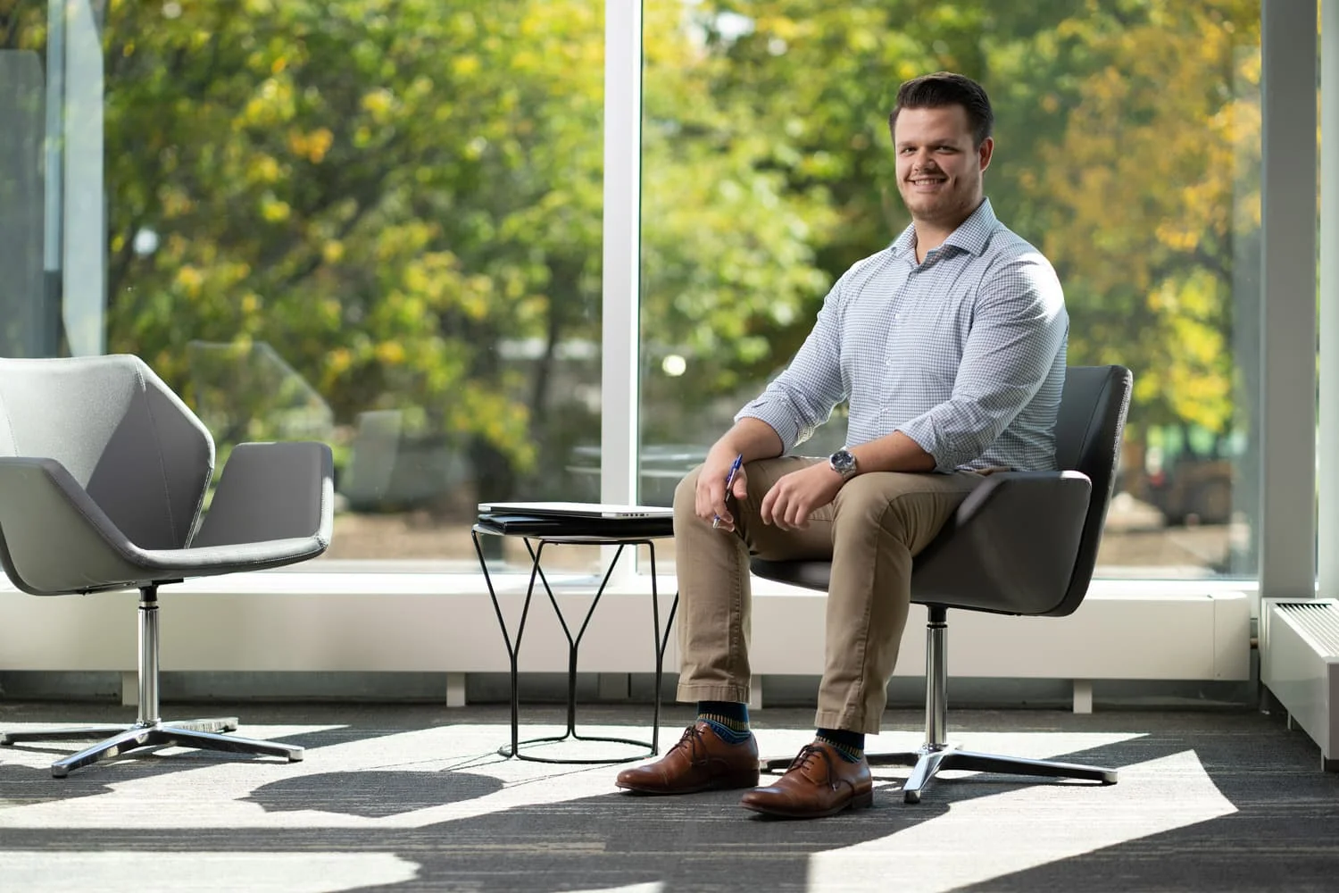 student sitting in chair in front of windows with trees outside.