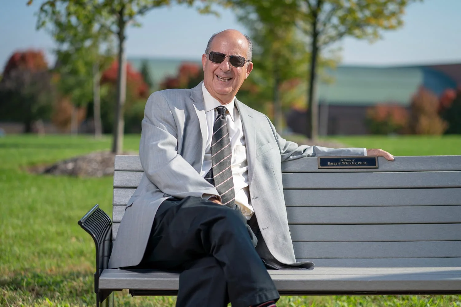 Doctor in sunglasses sitting on bench on campus.
