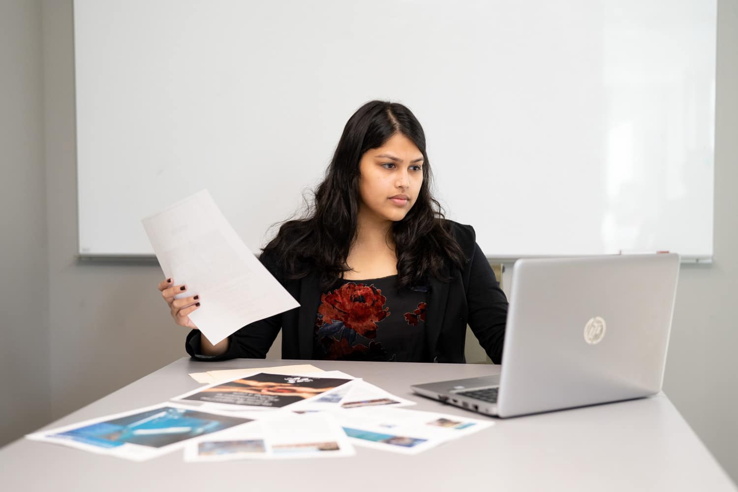  student holding paperwork while looking at macbook 