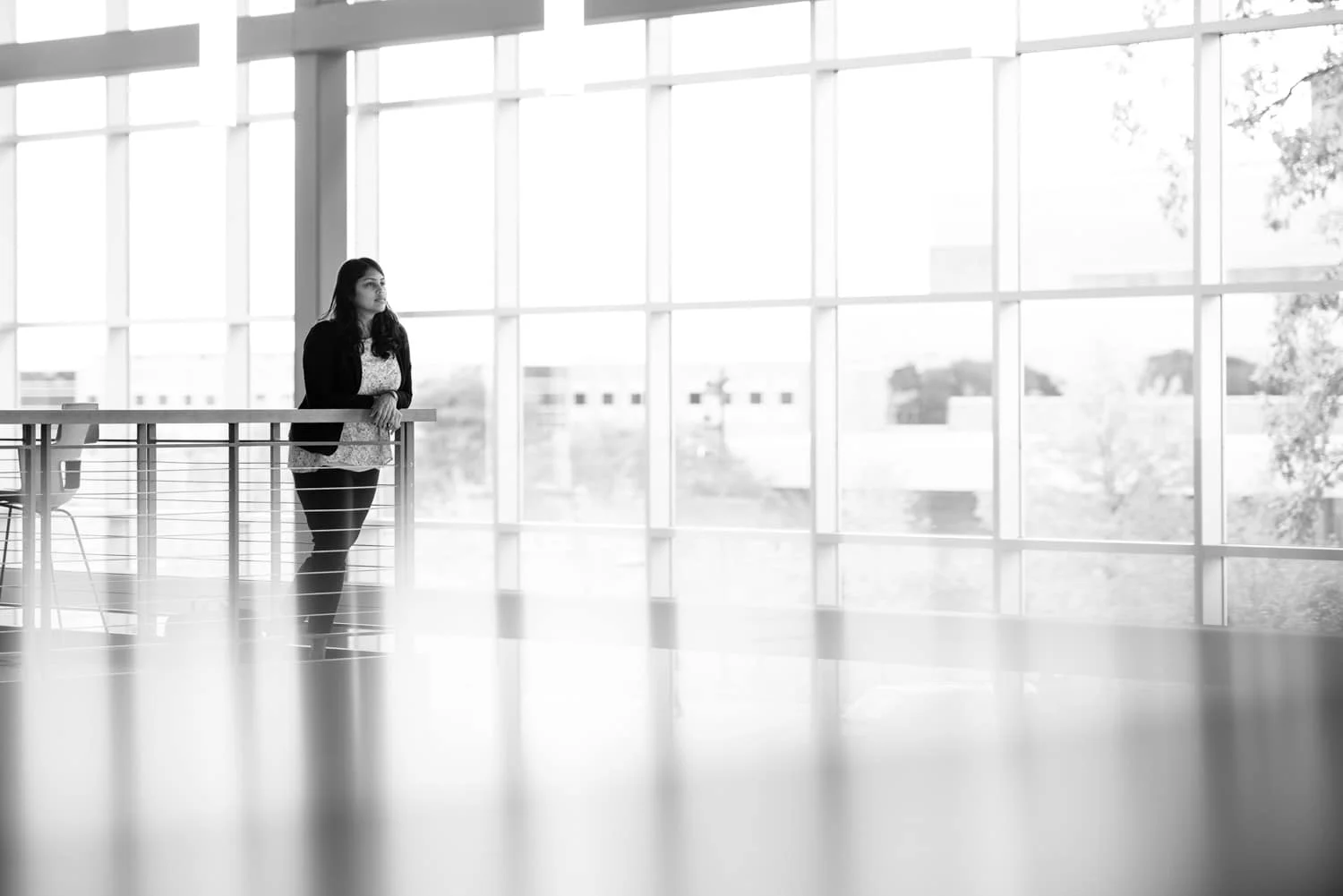 Student standing on ledge in room with big windows.