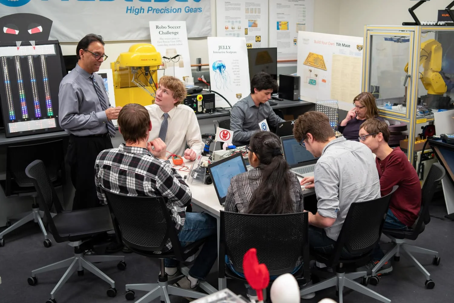 Professor and Oakland University students around a table working on various engineering projects.