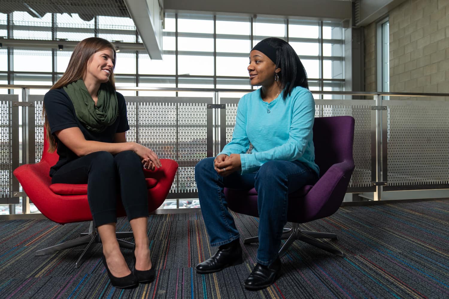  student and advisor talking in chairs in front of windows 