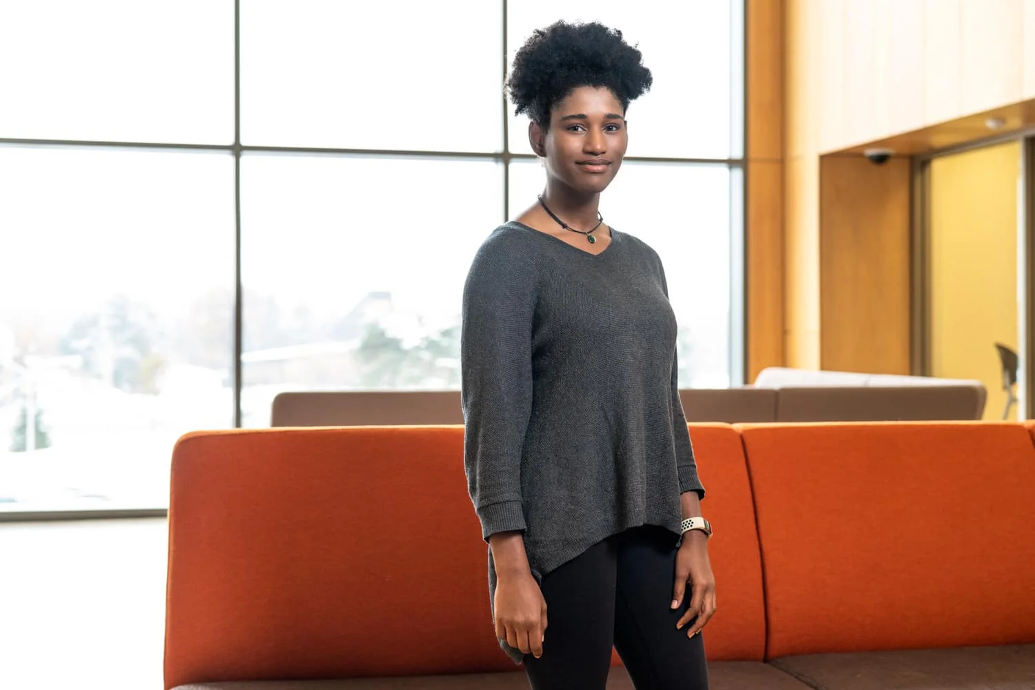 portrait of student standing in front of red couch and large windows