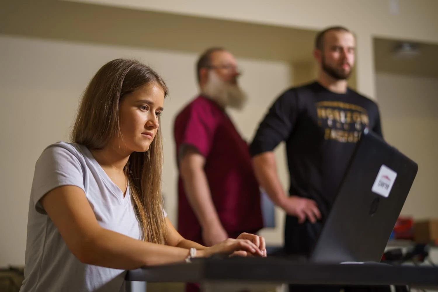 student on computer with athlete in background