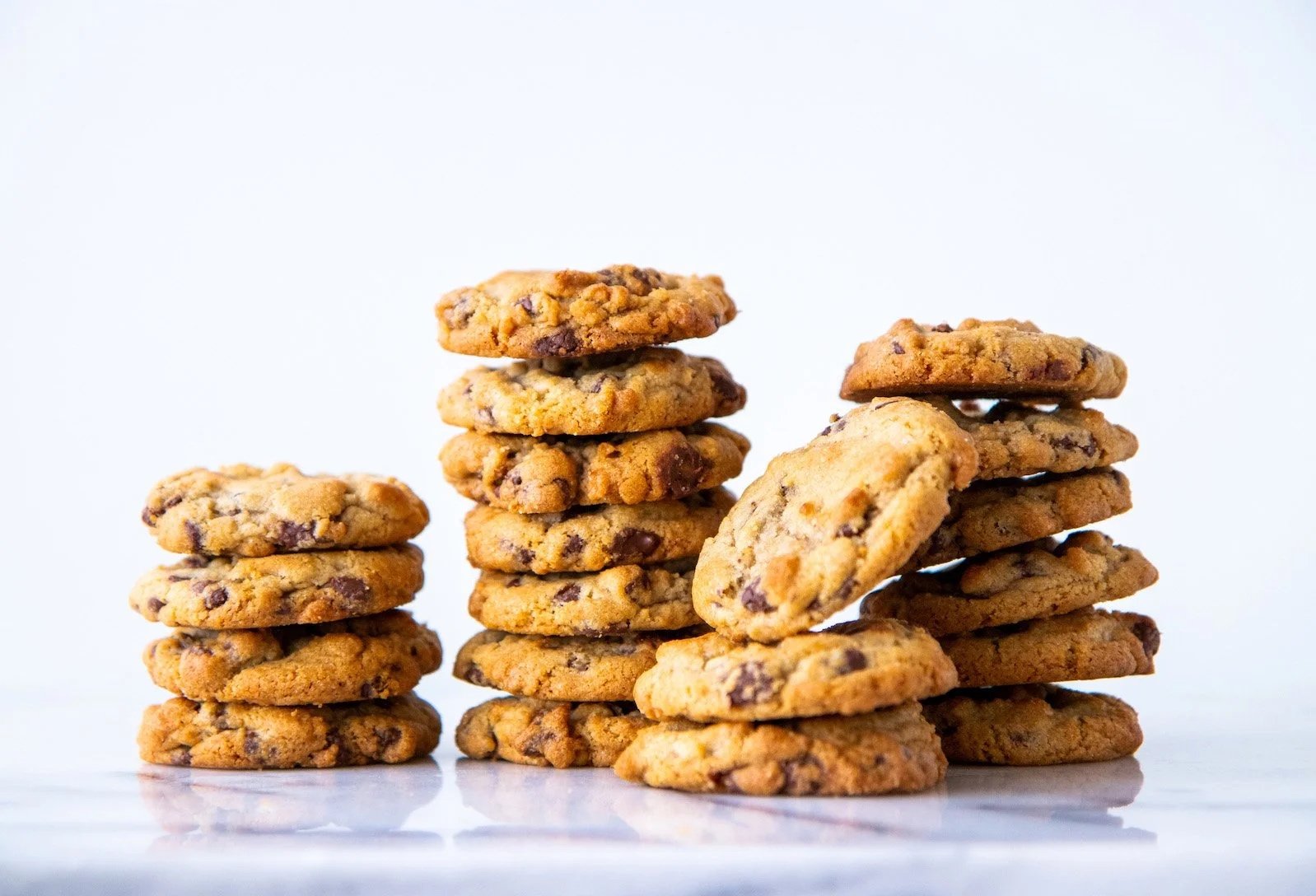 Stacks of chocolate chip cookies on a white surface against a plain white background.