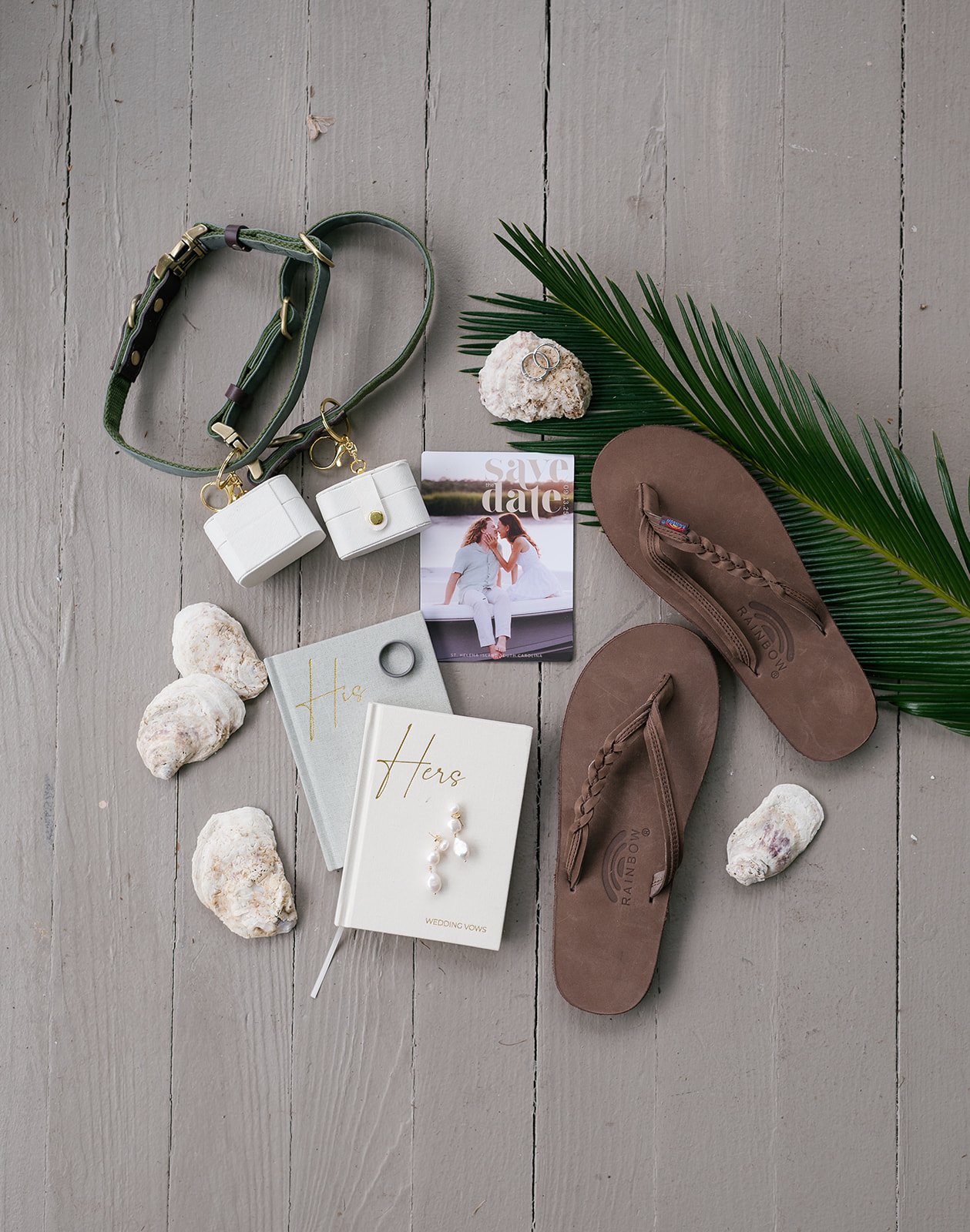 Wedding accessories and wedding vows on a wooden floor, including brown flip-flops, rings, a palm leaf, shells, a wedding vow booklet, and wedding photo.