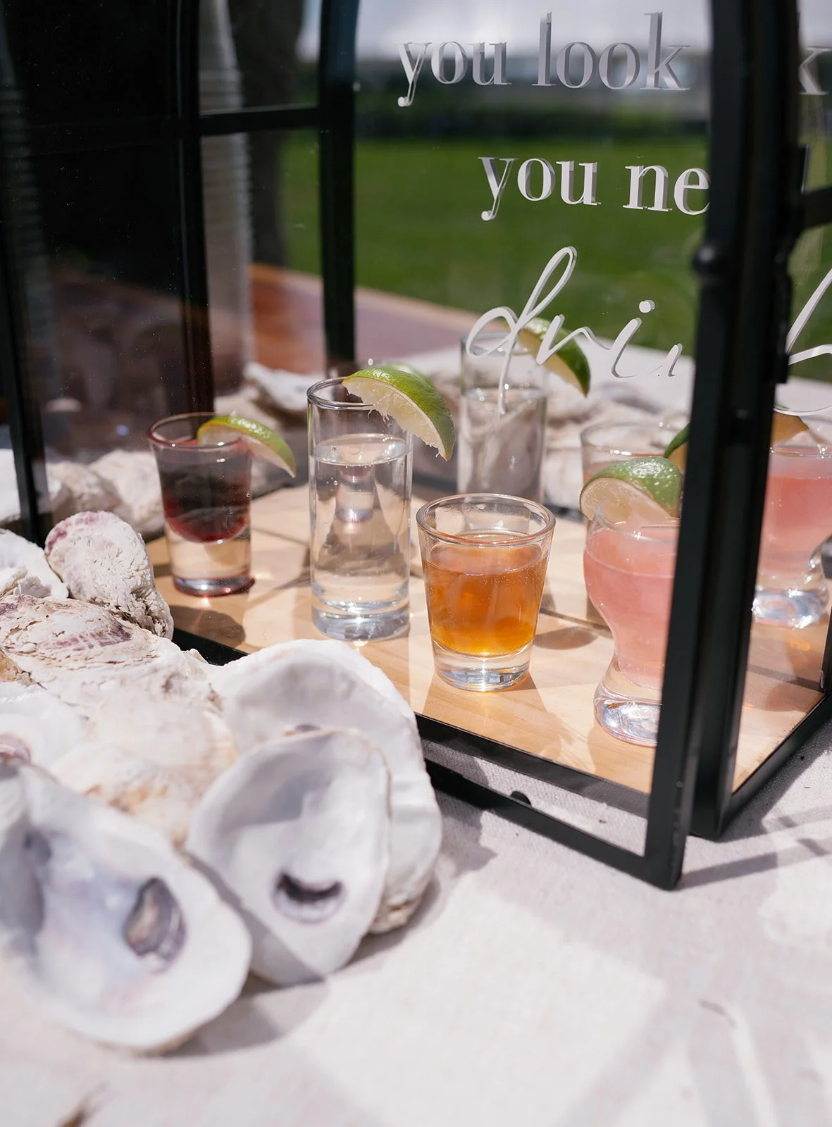 A display of assorted canned oysters and shot glasses with lime wedges, filled with different colored liquids, in a glass case with a quote on the glass reading 'you look you ne'.