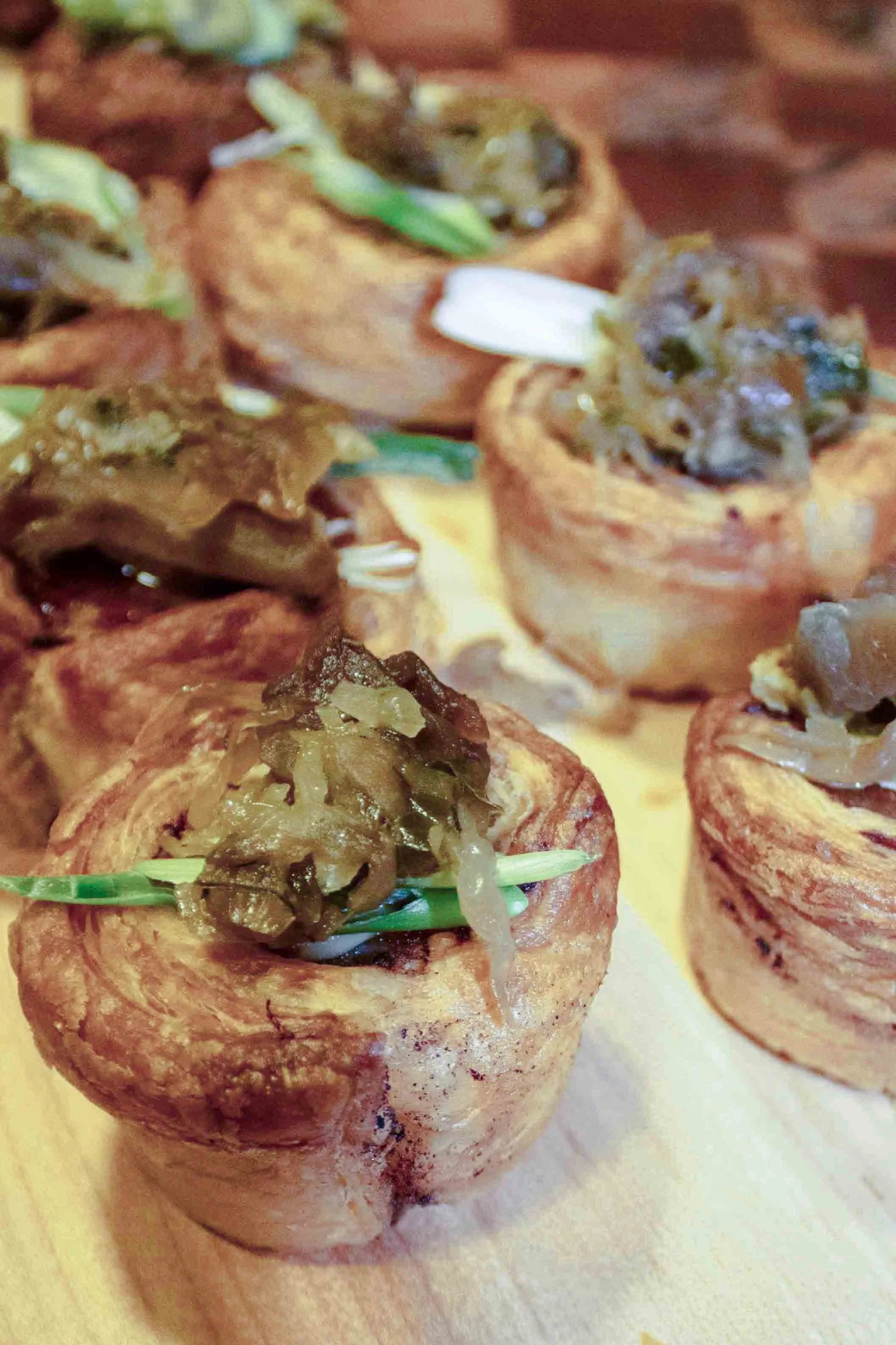 Close-up of several crispy fried appetizers topped with sautéed mushrooms and green onions on a wooden serving tray.