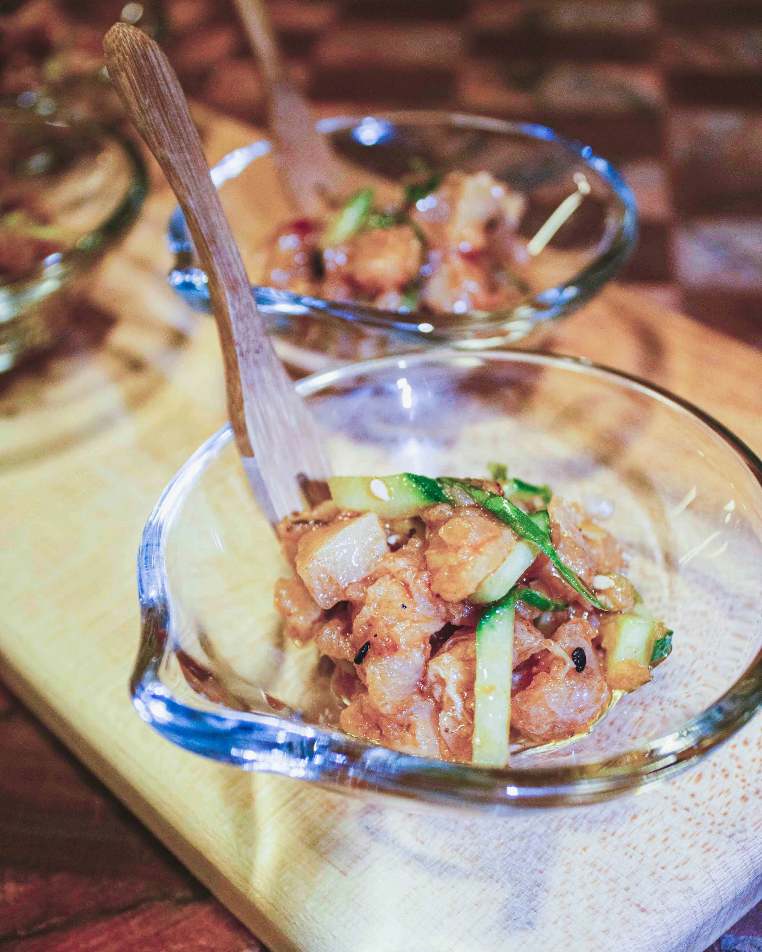 Close-up of a glass filled with kimchi, with a fork in the background. The kimchi appears to have green onions, sesame seeds, and chili flakes.