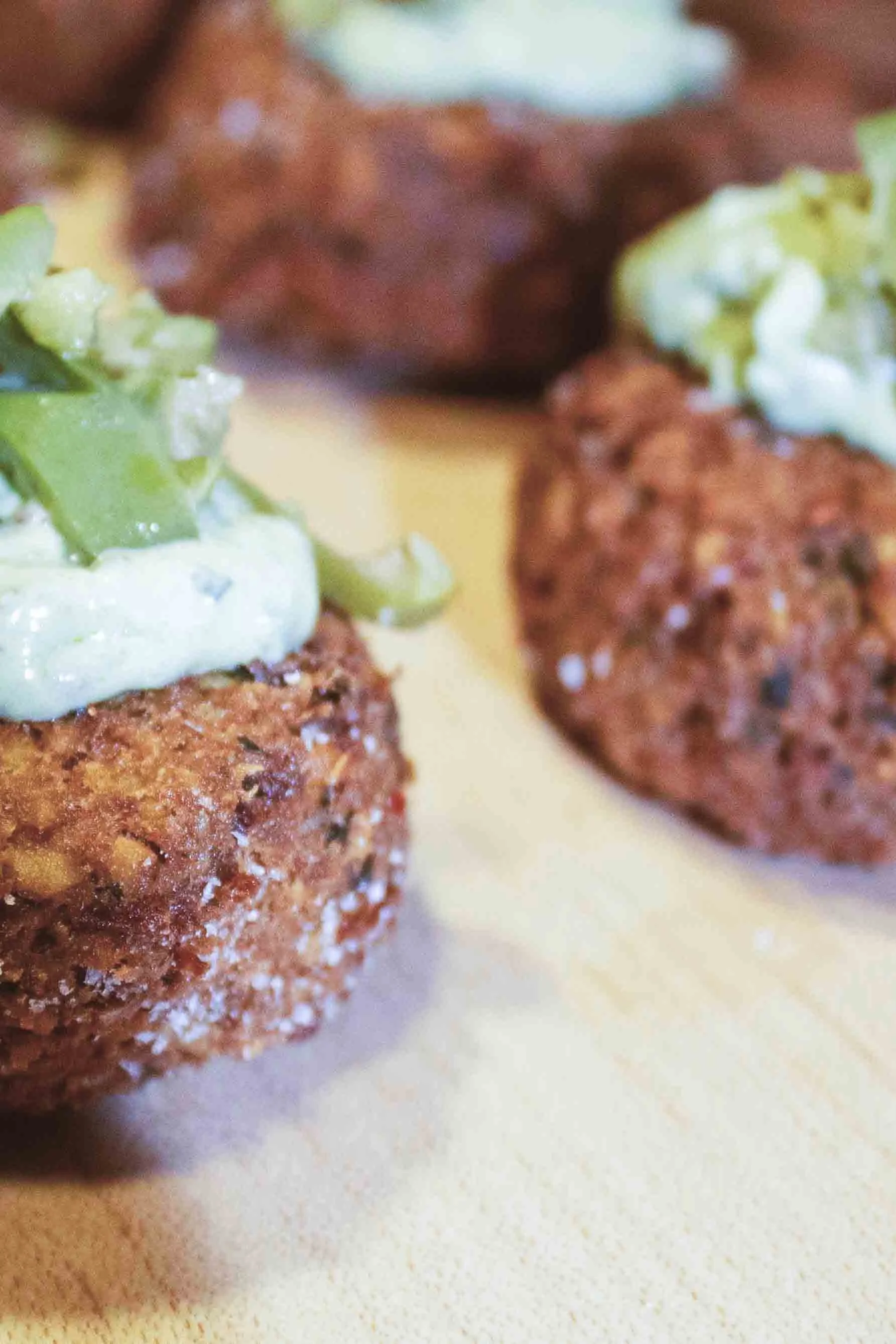 Close-up of three cooked beef patties with toppings, including chopped onions and possibly green peppers, on a light-colored surface.