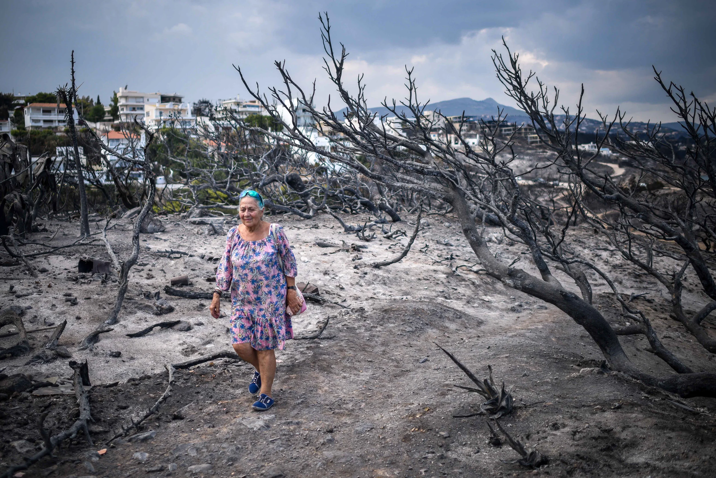  An elderly woman walks through an area of burnt bushes in Rafina, Greece after Wildfires ravaged houses and properties in the seaside resort. 