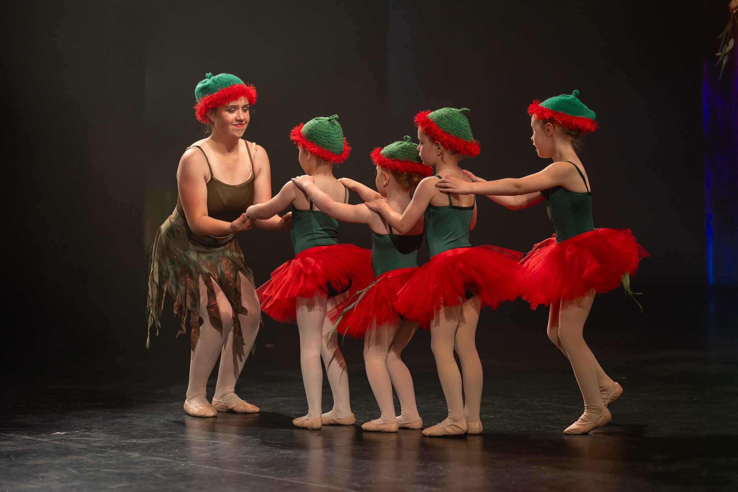 Young ballet dancers dressed as Christmas elves performing on stage with a teacher or director.