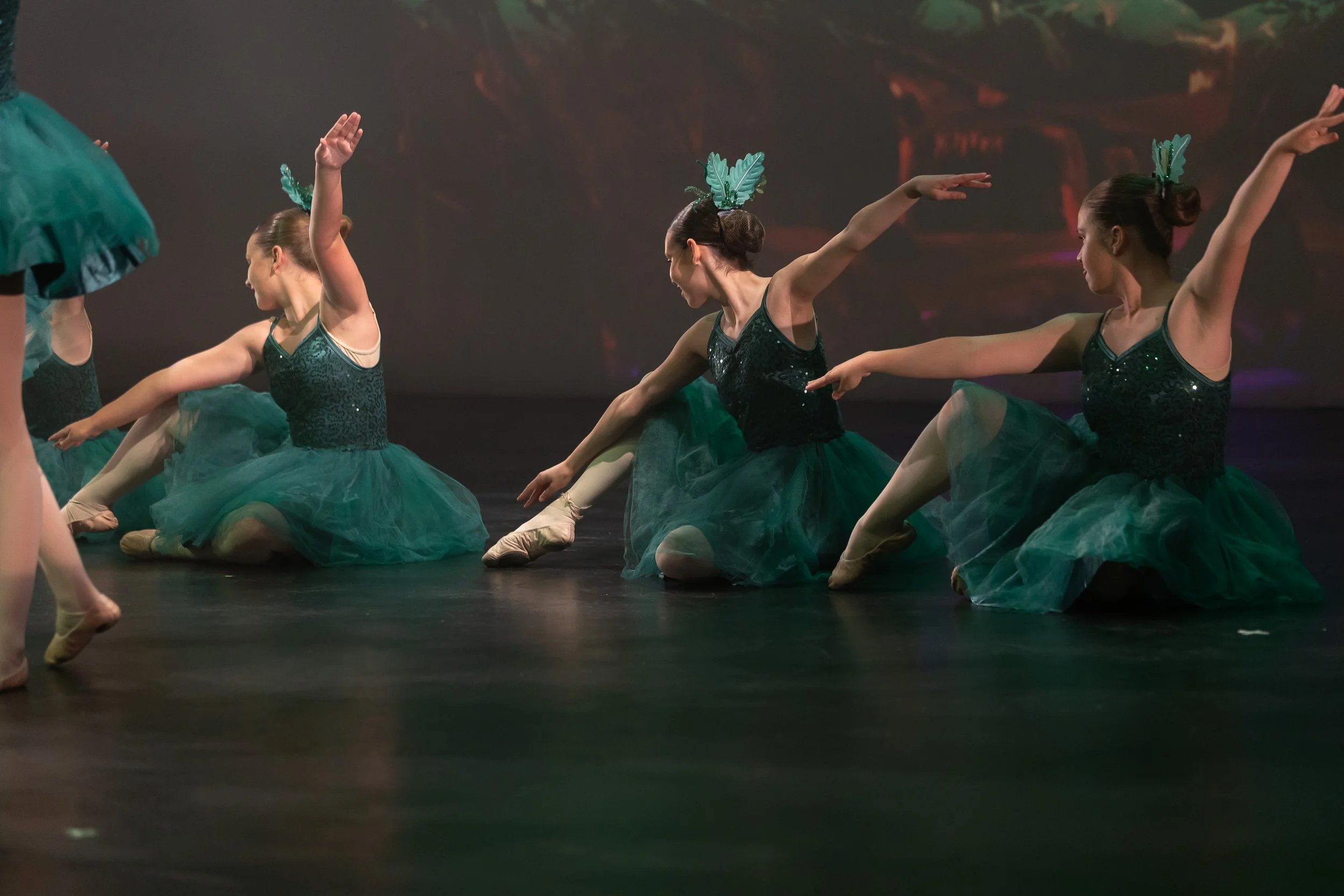 Ballet dancers dressed in green tutus and black sequined tops performing on stage.