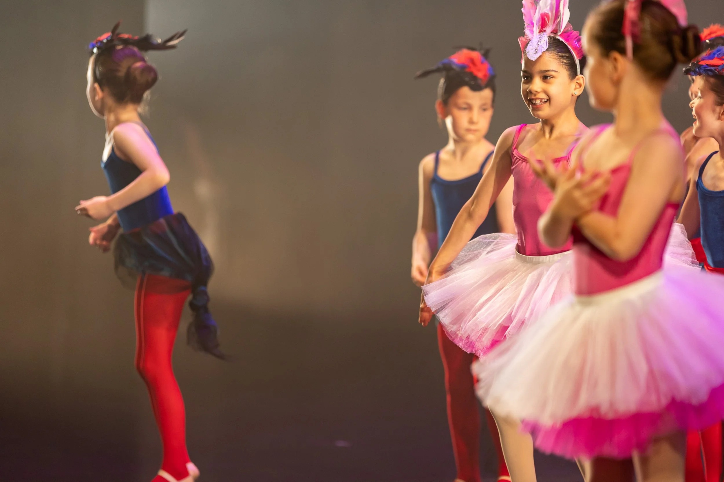 Young girls in colorful costumes and tutus preparing for a dance performance on stage.
