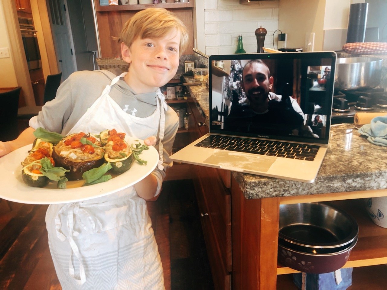 Young boy holding plate of food and smiling next to computer