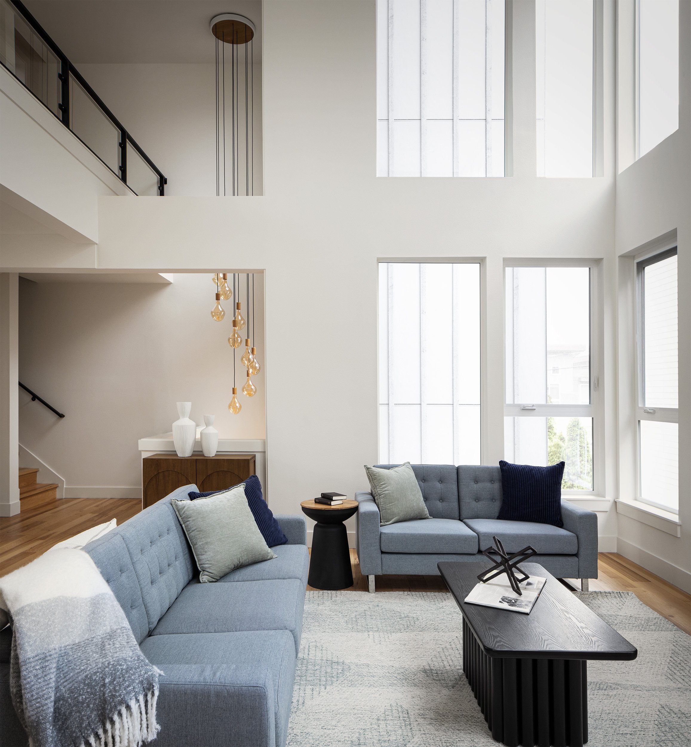 Bright double height residential living room interior in Seattle with blue sofas, tall windows, and modern pendant lighting, Seattle interior photography by Mike Arty