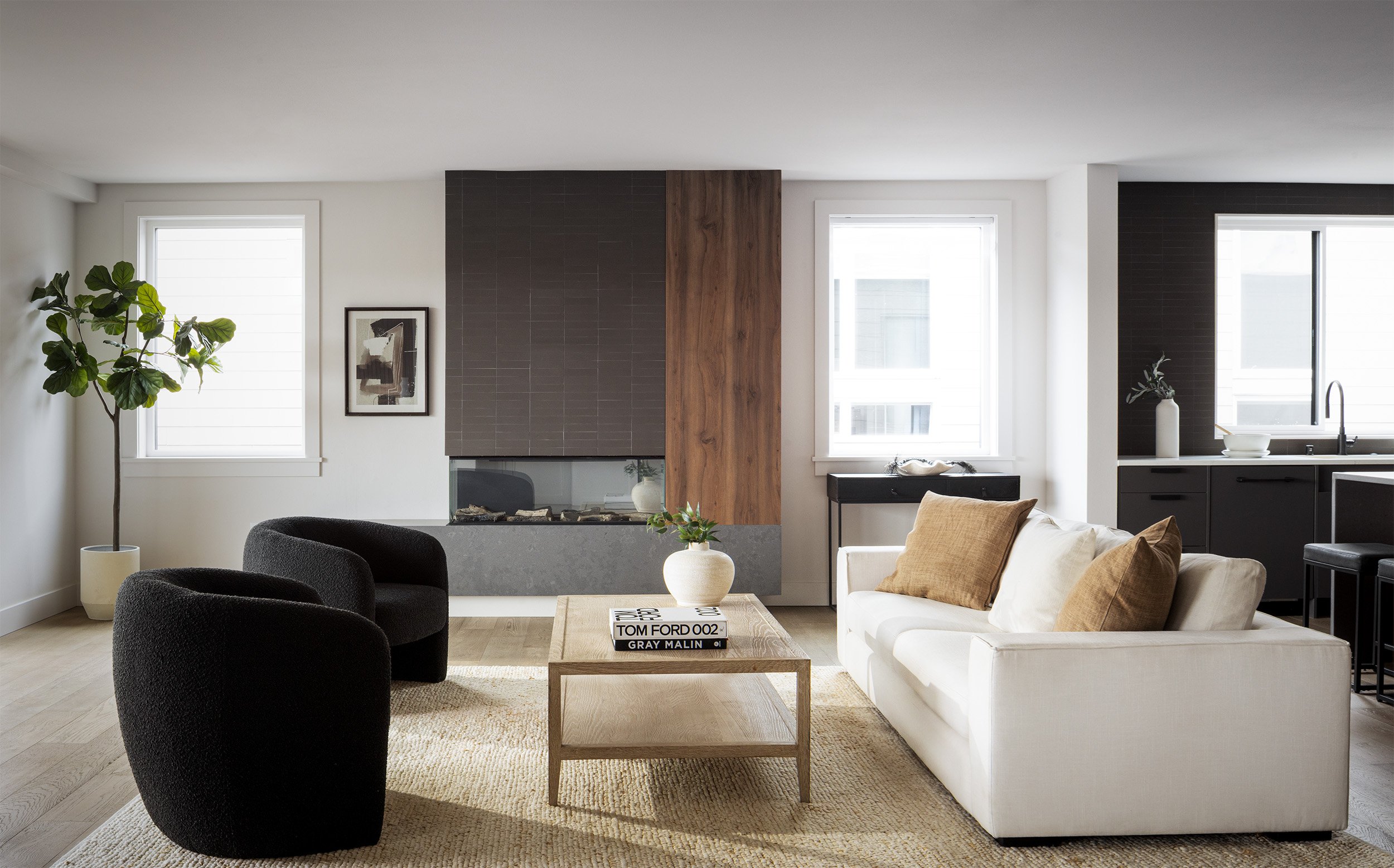 Contemporary open plan living room with white sofa, black boucle chairs, wood accent fireplace, and sleek kitchen.
