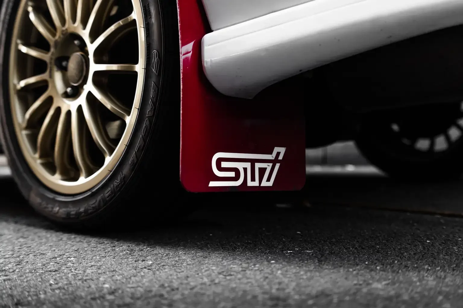 close up of gold OZ racing wheels and red sti mudflap on white gc8 subaru impreza WRX STi version 4 1998 JDM vehicle for export sale New Zealand