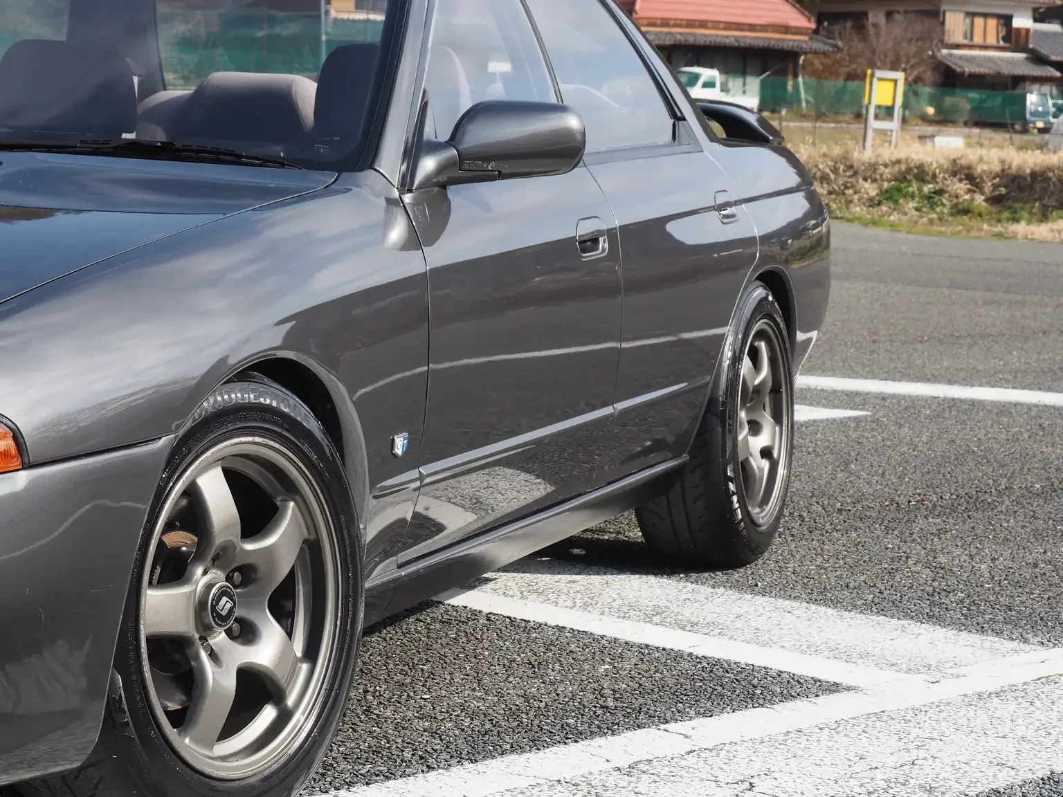 Front passengers low side view of a grey 1991 Nissan Skyline GTS25 Type X G 4 Door Sedan with GTR wheels for export from Japan