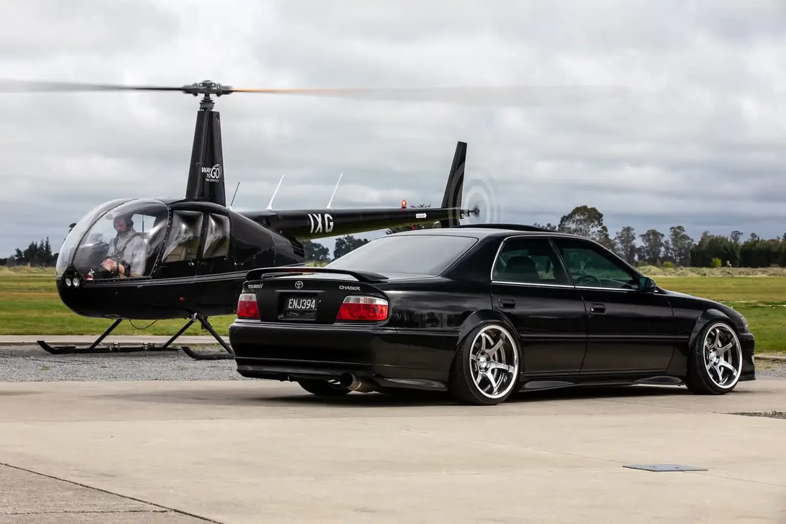 passenger rear end view with helicopter on pad black toyota chaser tourer v jzx100 custom steel wide body jdm export vehicle new zealand