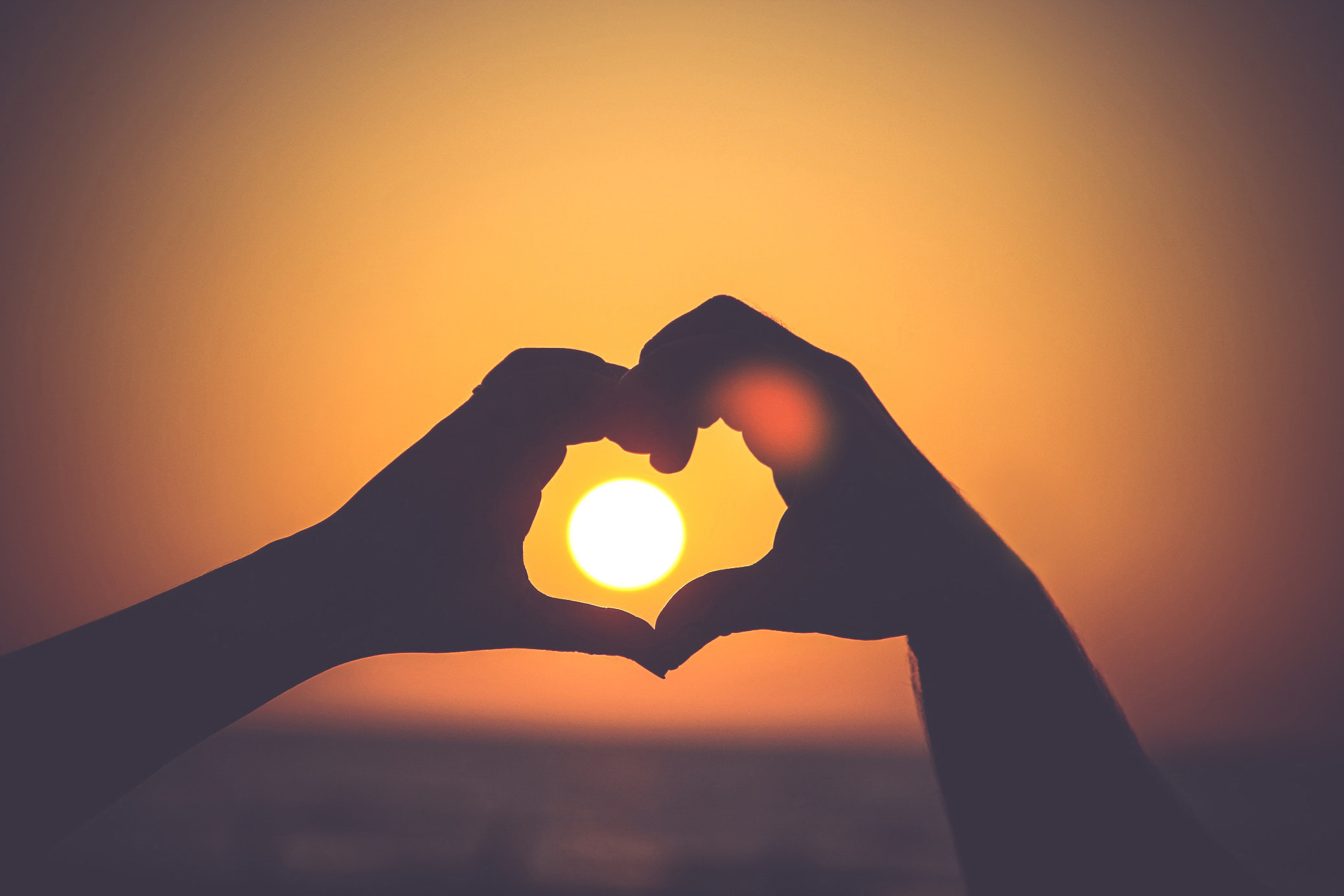 Hands forming a heart around the setting sun representing healing, hope, and individual psychotherapy in Toronto and online across Ontario.