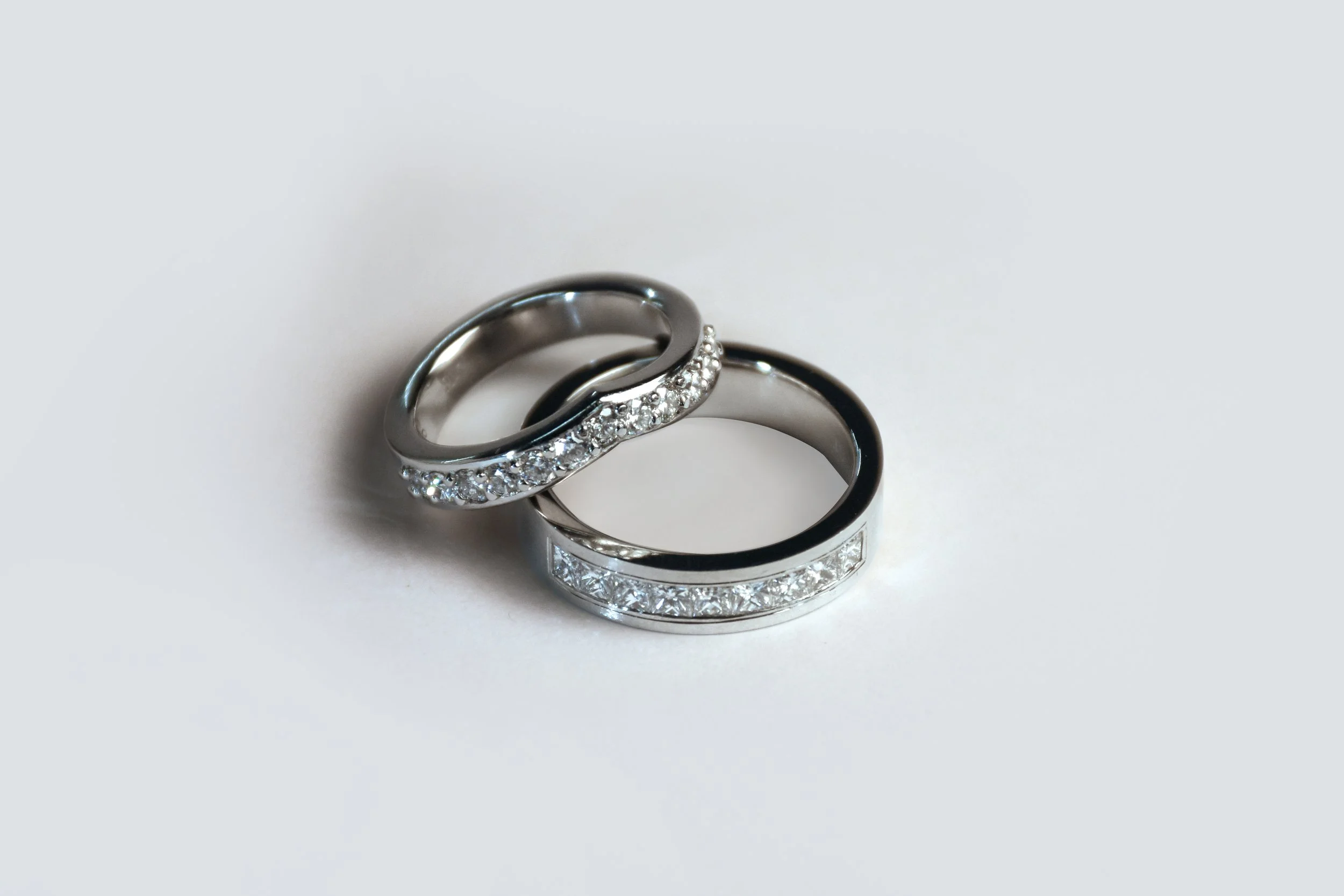 Two silver rings, one with embedded diamonds and one with a pattern of small diamantés, on a white surface.