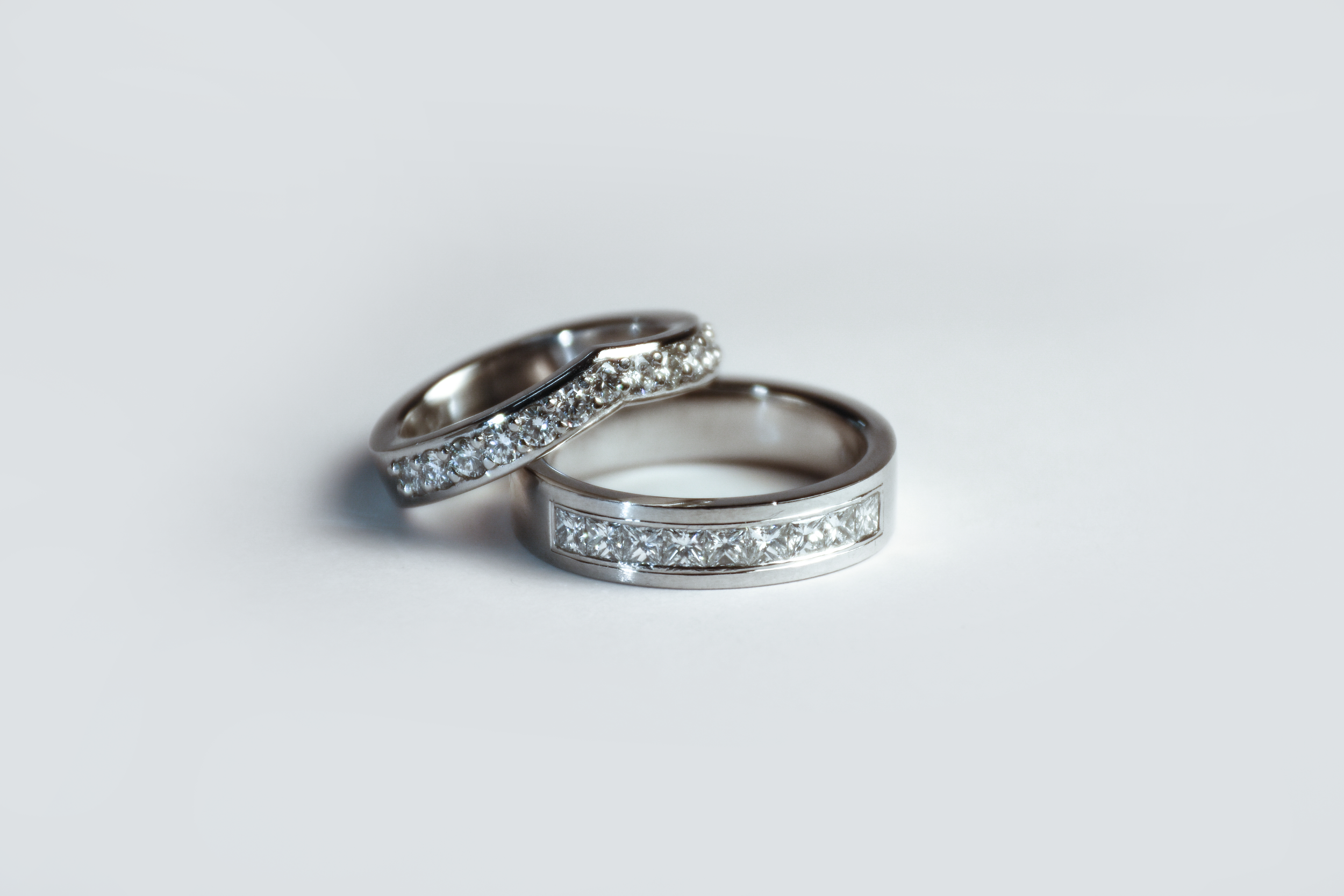Two silver rings with embedded diamonds placed on a white surface.