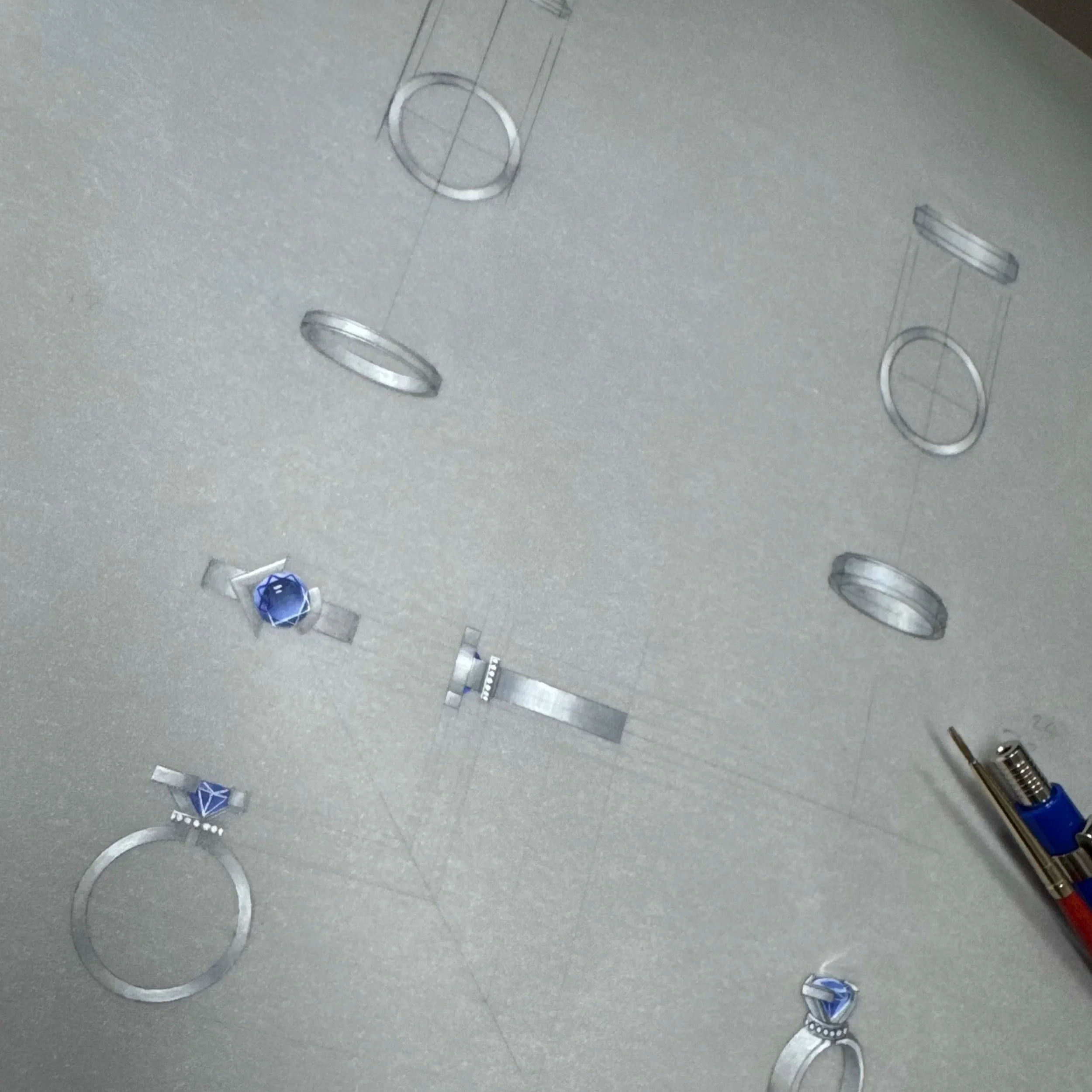 Design sketches of rings and jewelry components on paper with a pen nearby.