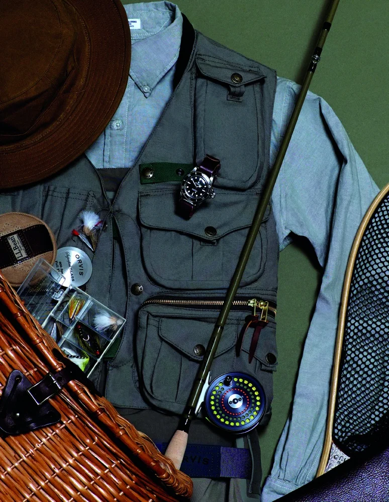 Guide vest and original hat FILSON, button-down shirt ENGINEERED GARMENTS, silver sonic convertible top waders, landing net, superfine glass fly rod, fly wallet, and cfo reel ORVIS, classic trout knife, fly box, and wicker creel L.L.BEAN red submariner watch ROLEX available at manoftheworld.com