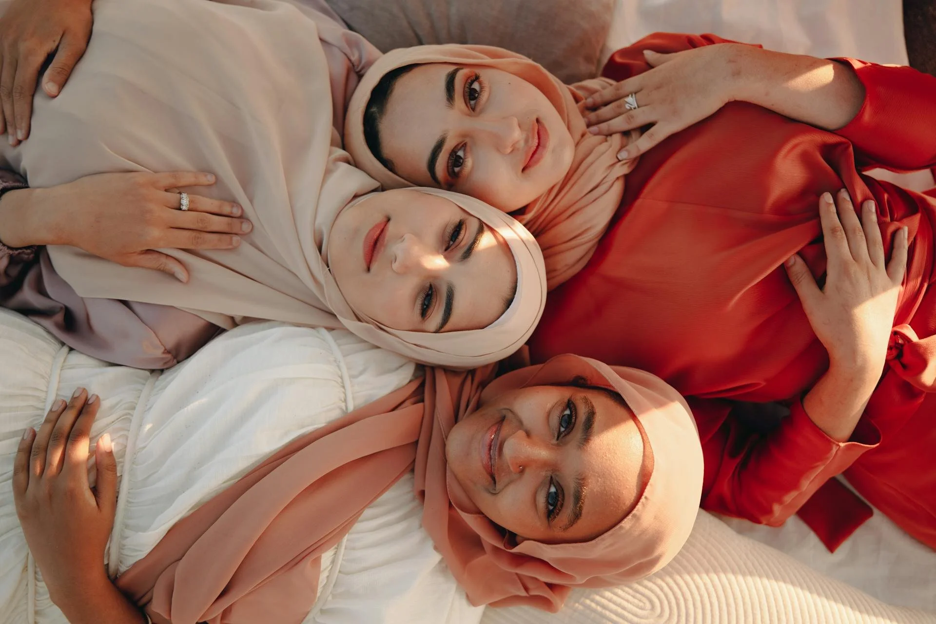 pexels-pnw-prod-8995949-Three women in hijabs, dressed in warm tones, lying together and embracing..jpg