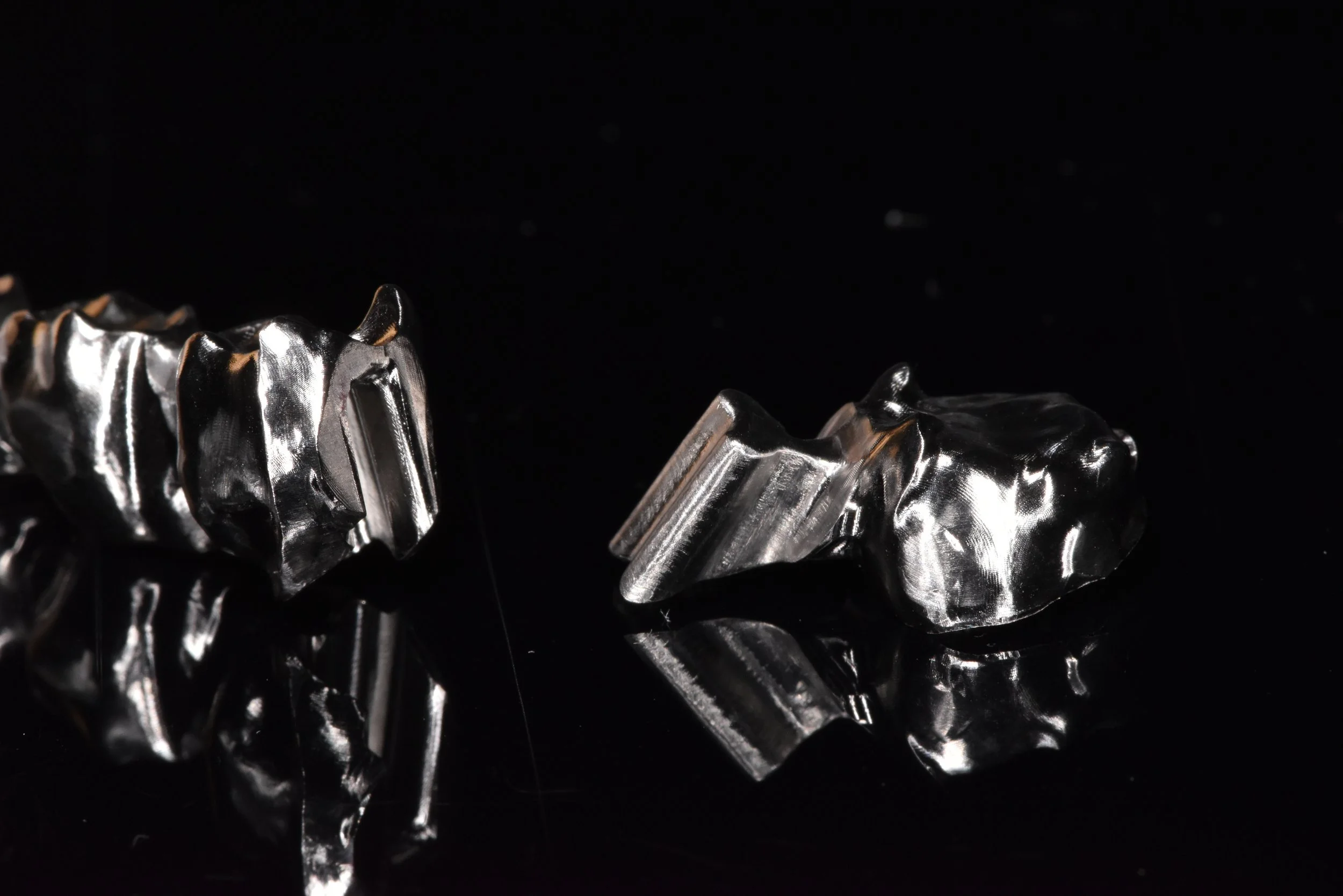 Zwei silberne Zahnkronen oder Zahnersatzteile auf schwarzem Hintergrund gespiegelt.