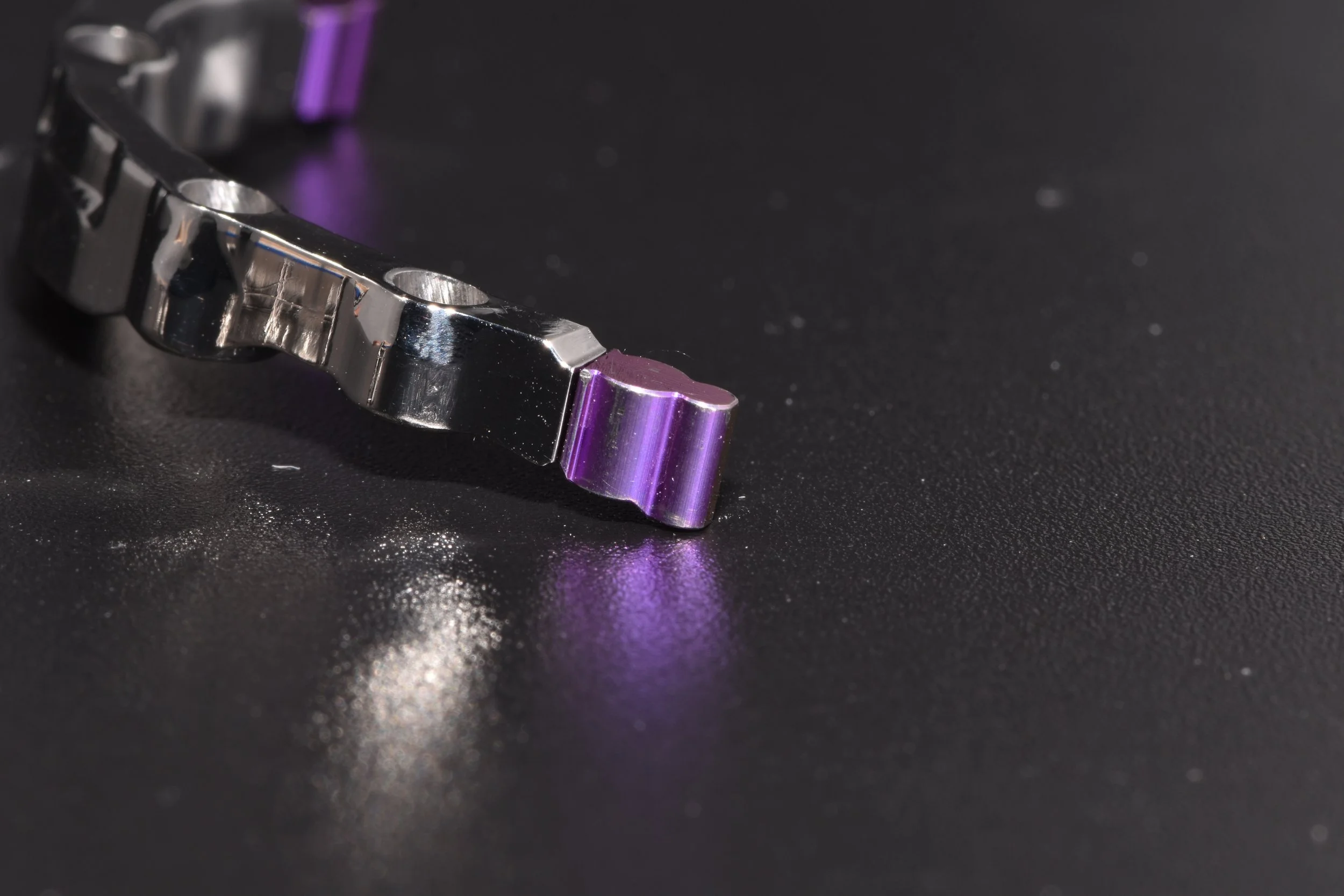 Nahaufnahme eines silbernen und violetten Metallobjekts auf schwarzem Hintergrund.