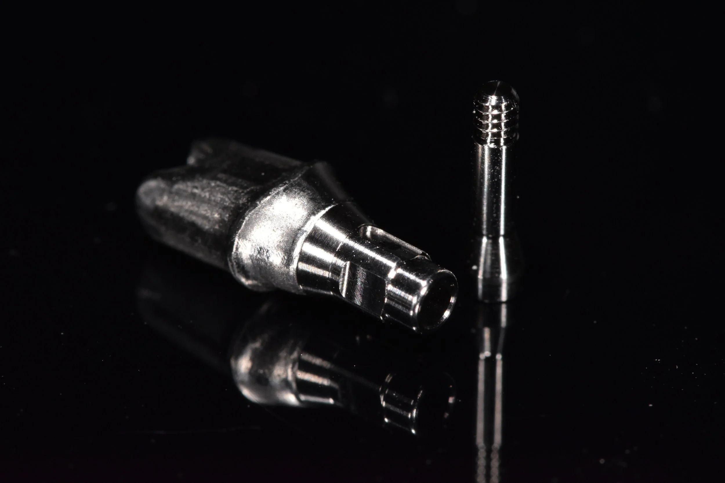 Zwei Metallteile, wahrscheinlich ein Zahnimplantatkomponenten, auf schwarzem Hintergrund.