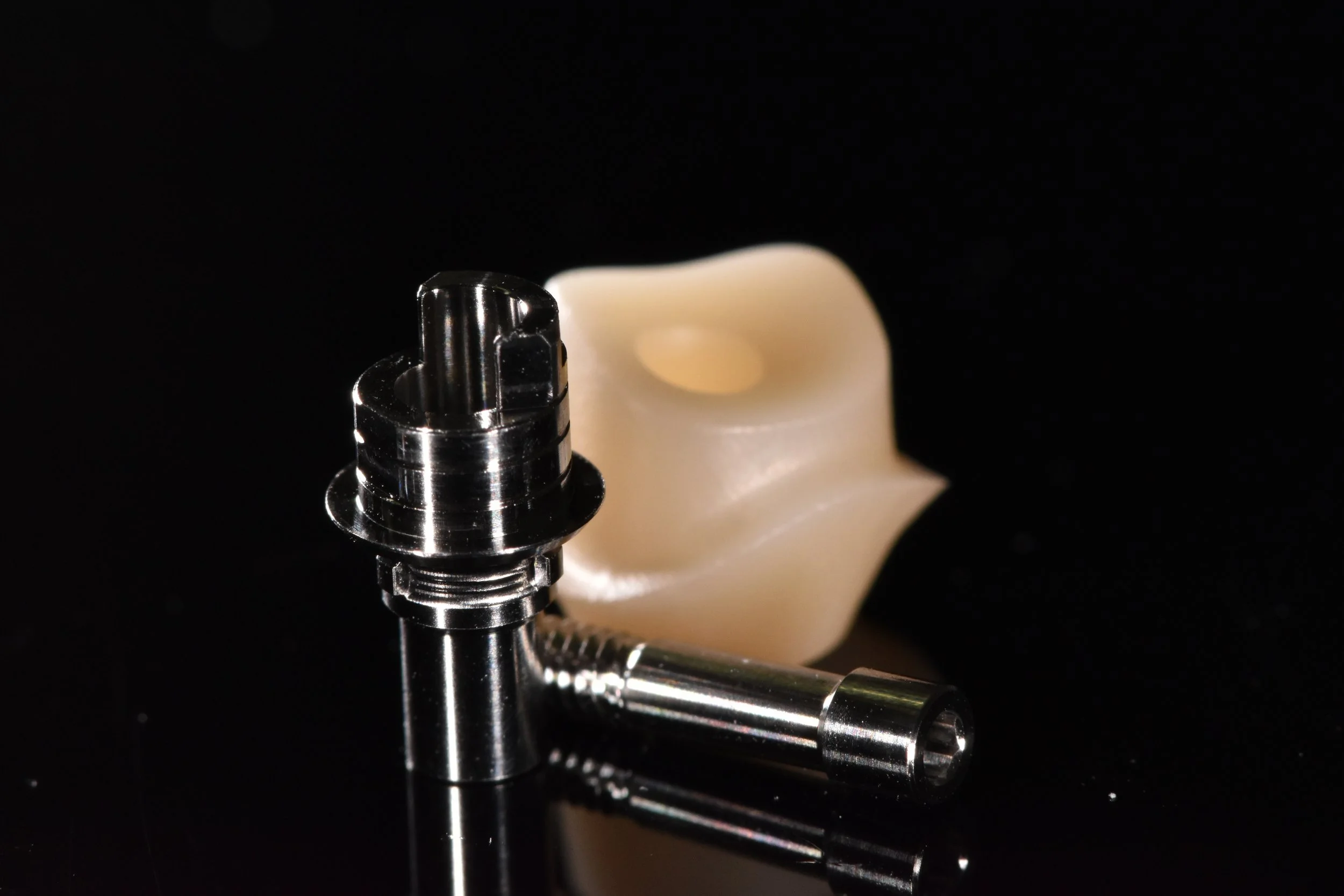 Nahaufnahme eines Metallteils mit Gewinde und beige Kunststoffkomponente auf schwarzem Hintergrund.