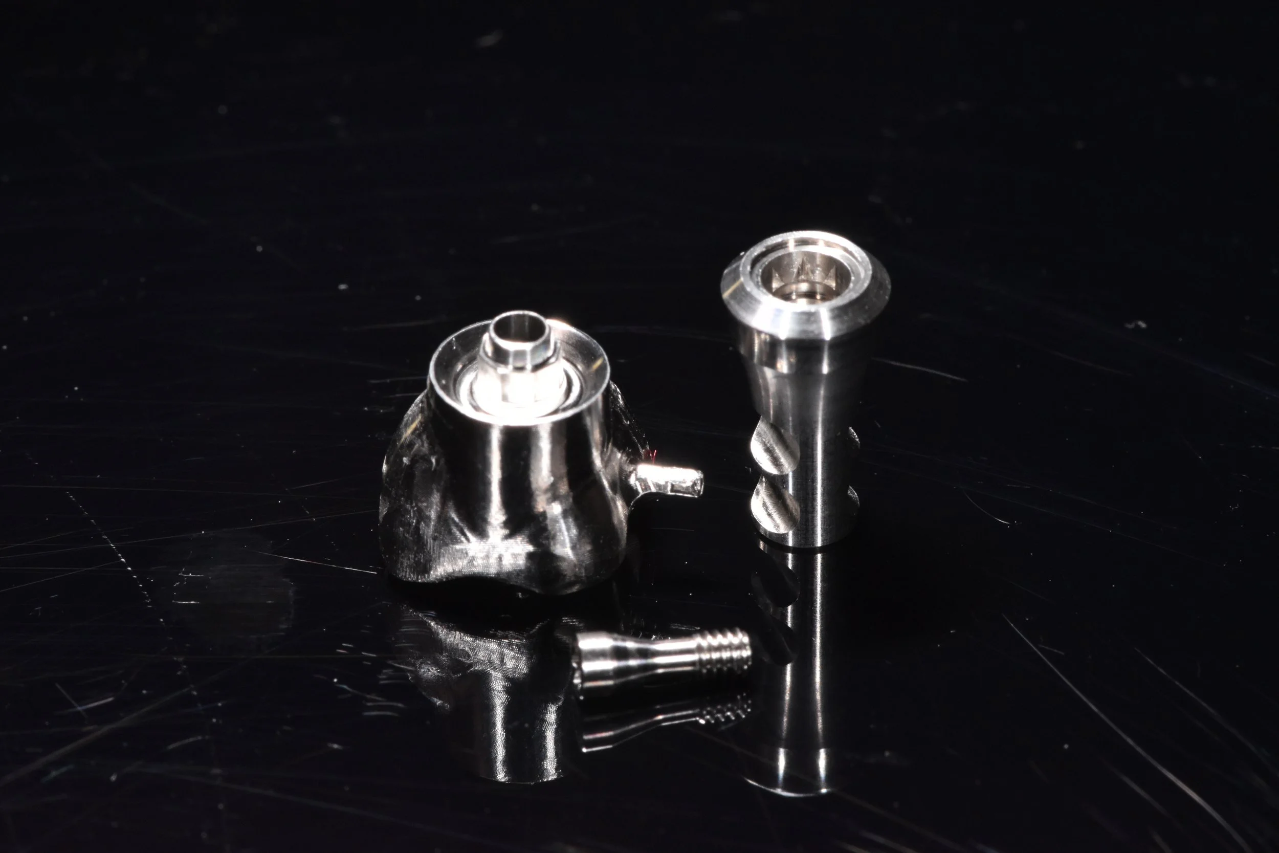 Metallische Zahnimplantatkomponenten auf schwarzem Hintergrund.