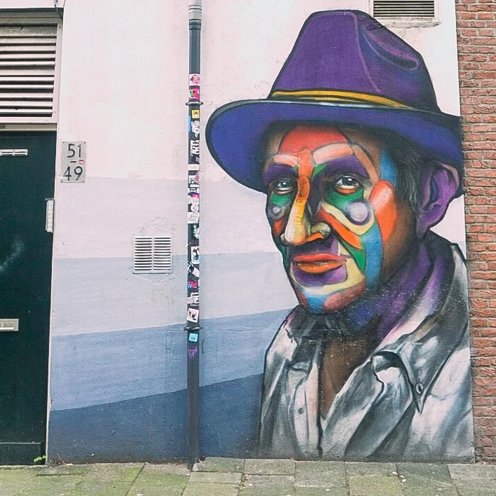 Rotterdam Street Art. Man with purple hat and face painted in many colours including red, yellow green and purple. Witte de WIthstraat.