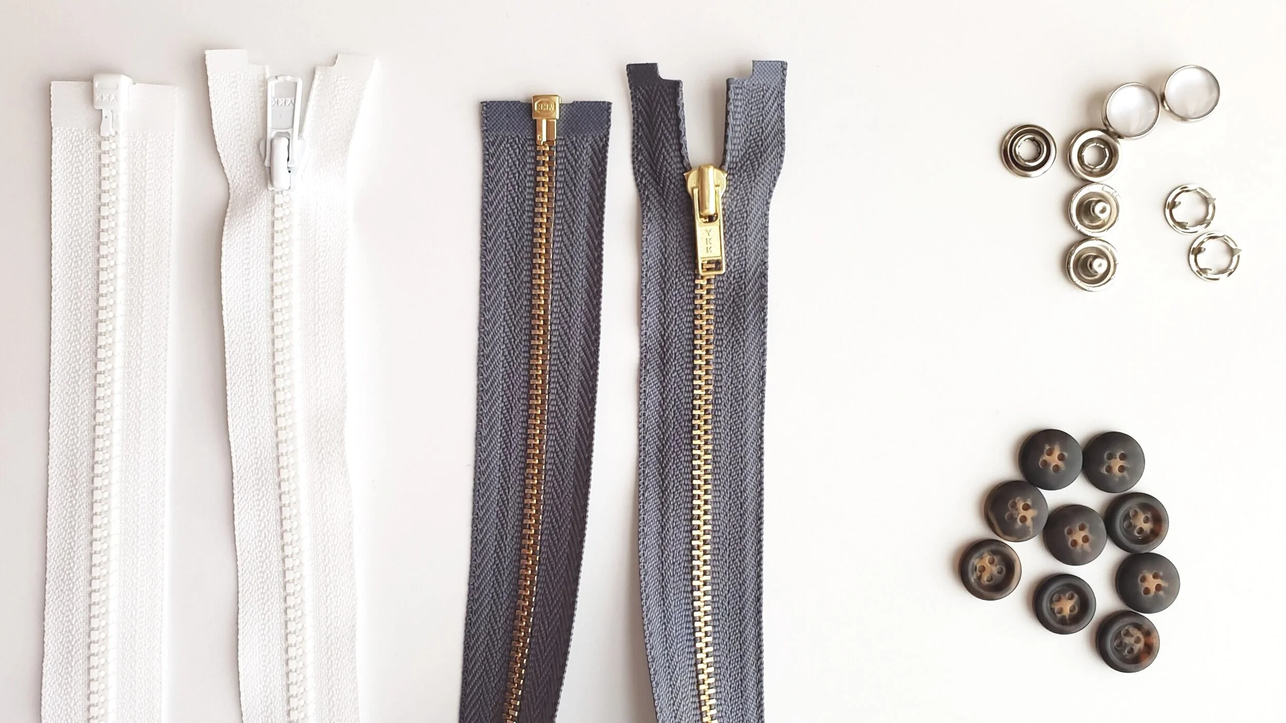 Left to right: #3 molded plastic separating jacket zipper, #3 brass separating jacket zipper, pearl snaps (top), and plastic buttons (bottom)