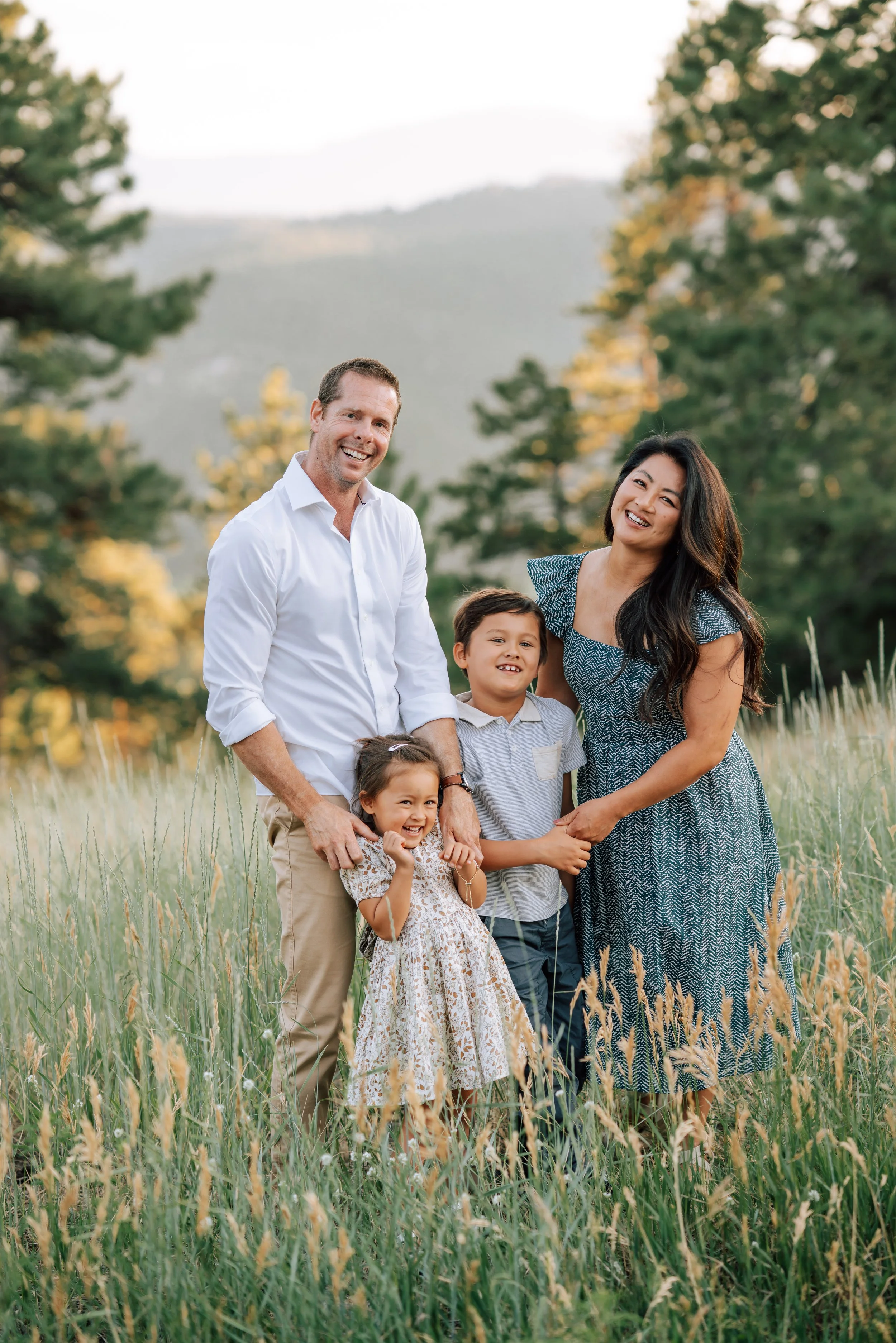 Aunt and Uncle with niece and nephew surrounded by tall summer grass with pine trees and Colorado mountains in the background at Mount Falcon.